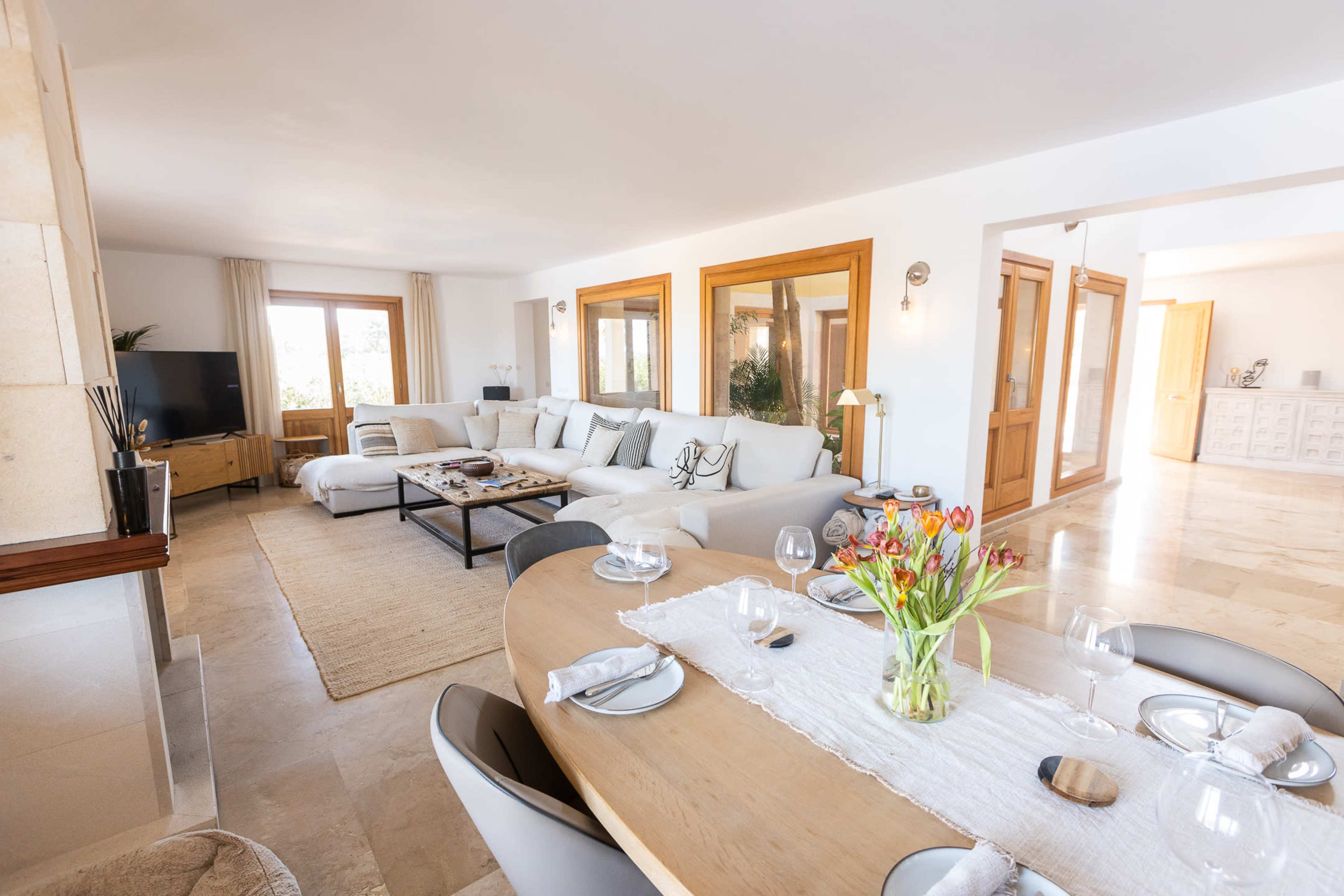 A bright, open-concept living space features a cozy sofa area, a dining table set for a meal, and large windows allowing natural light to fill the room.