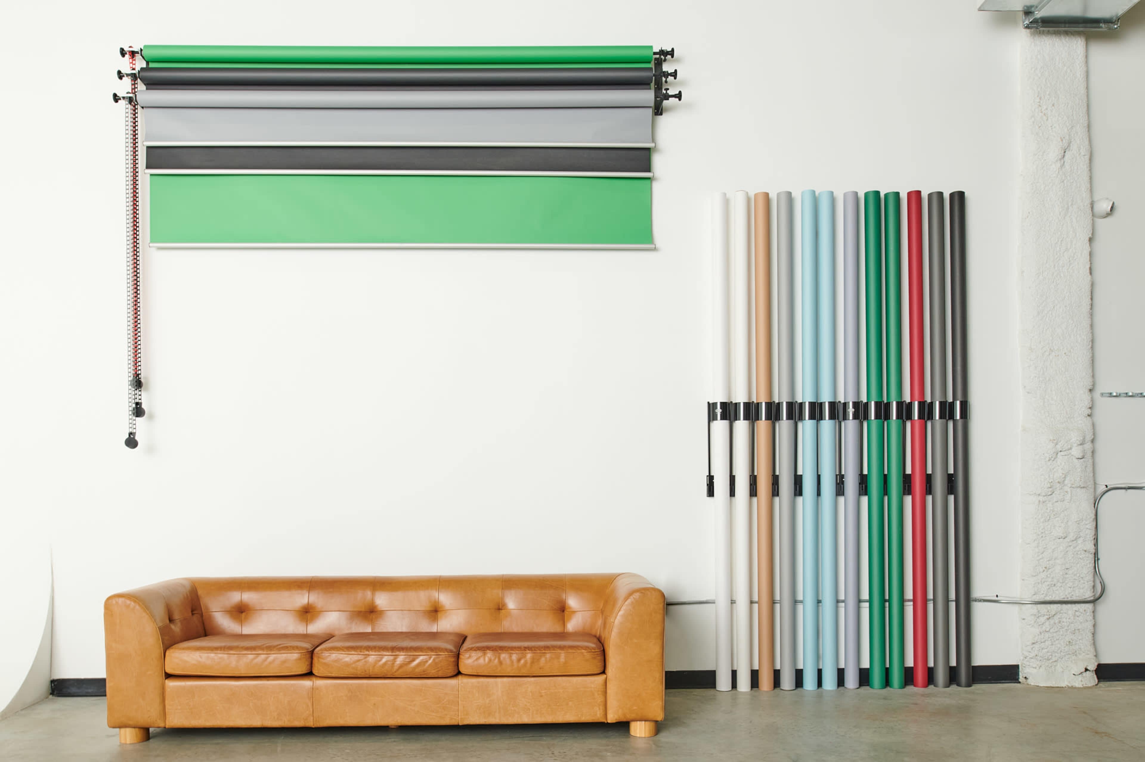 A brown leather sofa sits in front of a wall displaying various backdrops and rolls of colored paper.