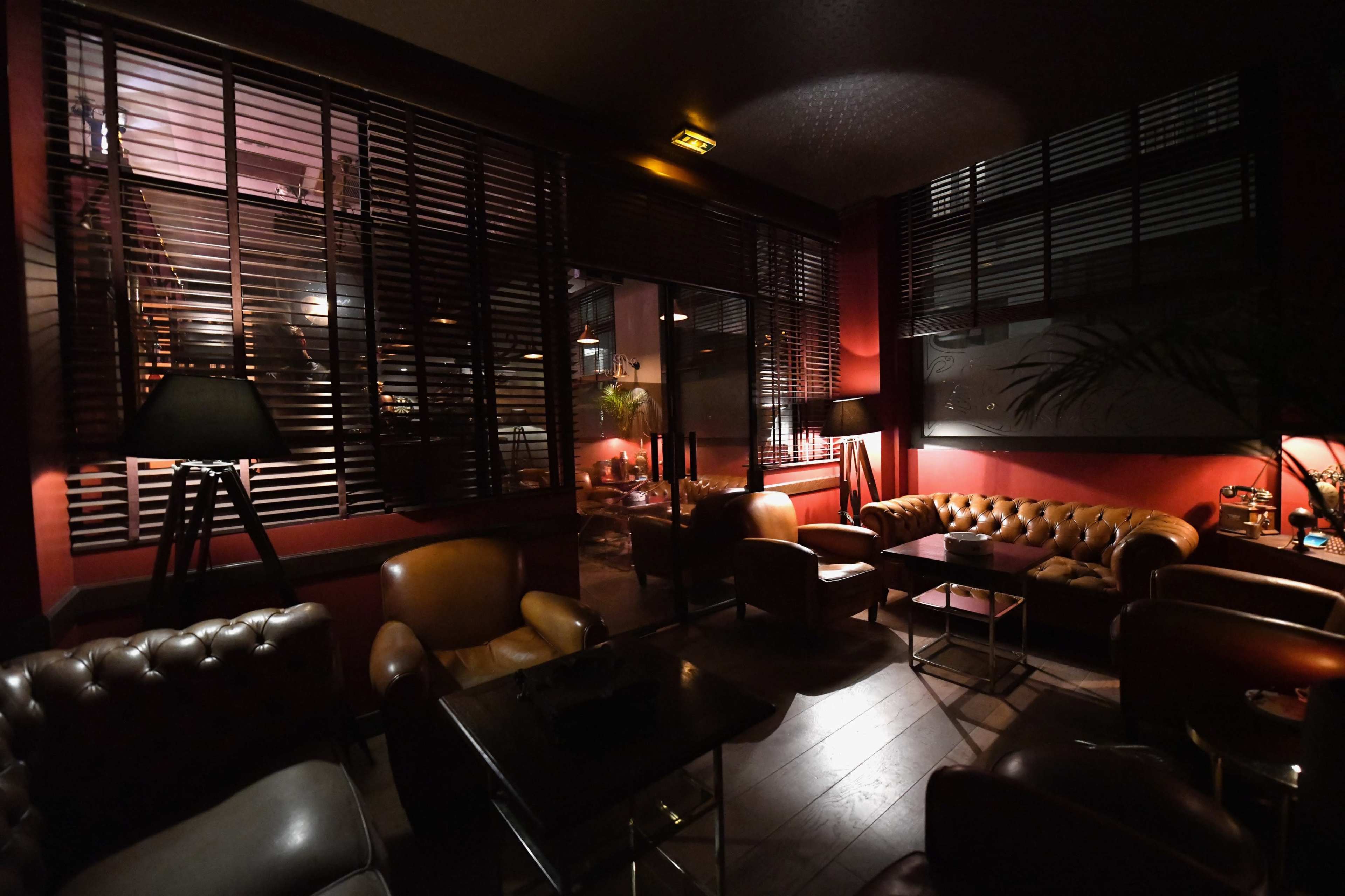 A cozy lounge area with leather sofas, low lighting, and large windows partially covered by wooden blinds.