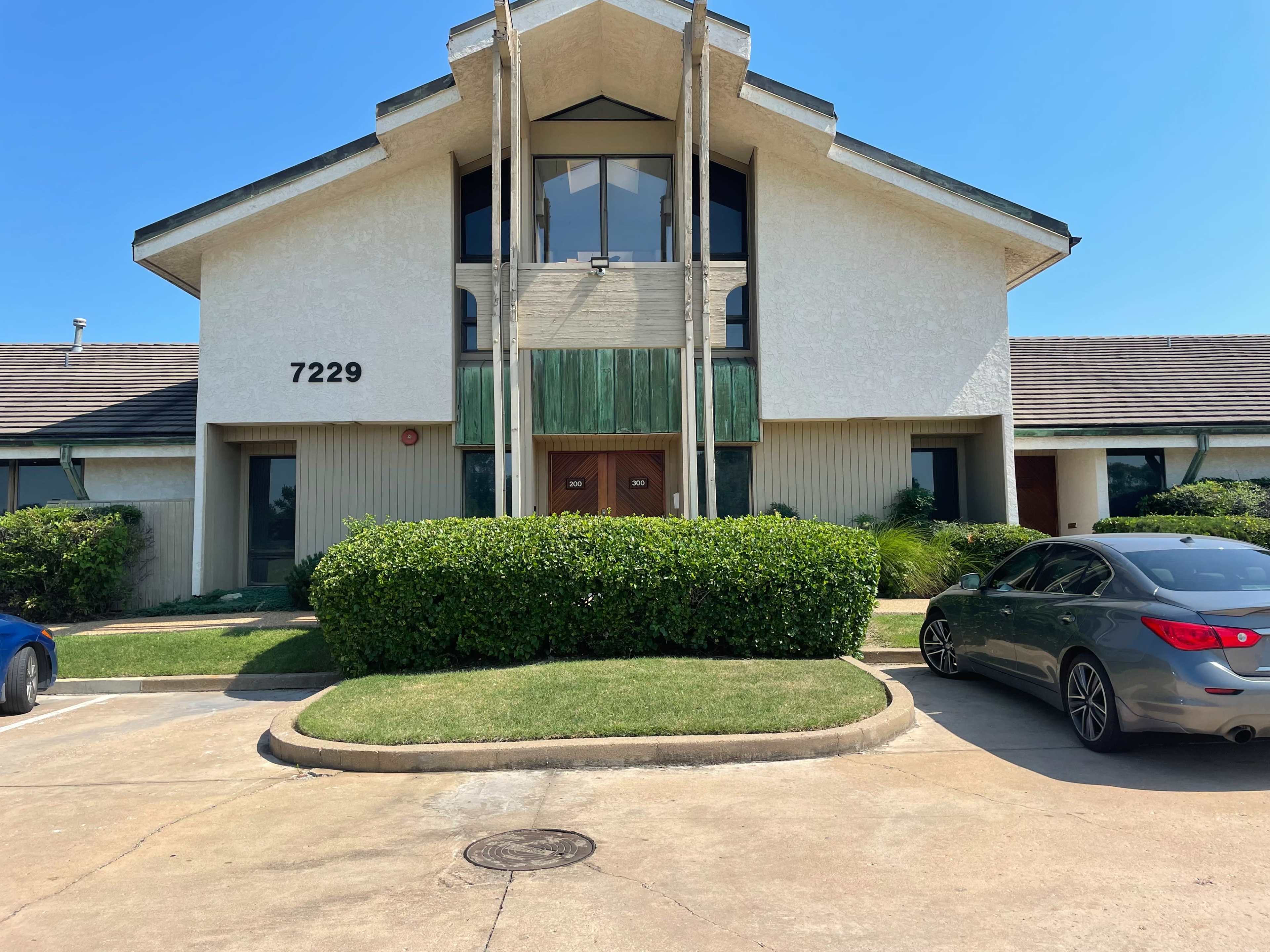 A two-story commercial building with a green entrance, flanked by parking spaces and well-maintained landscaping.