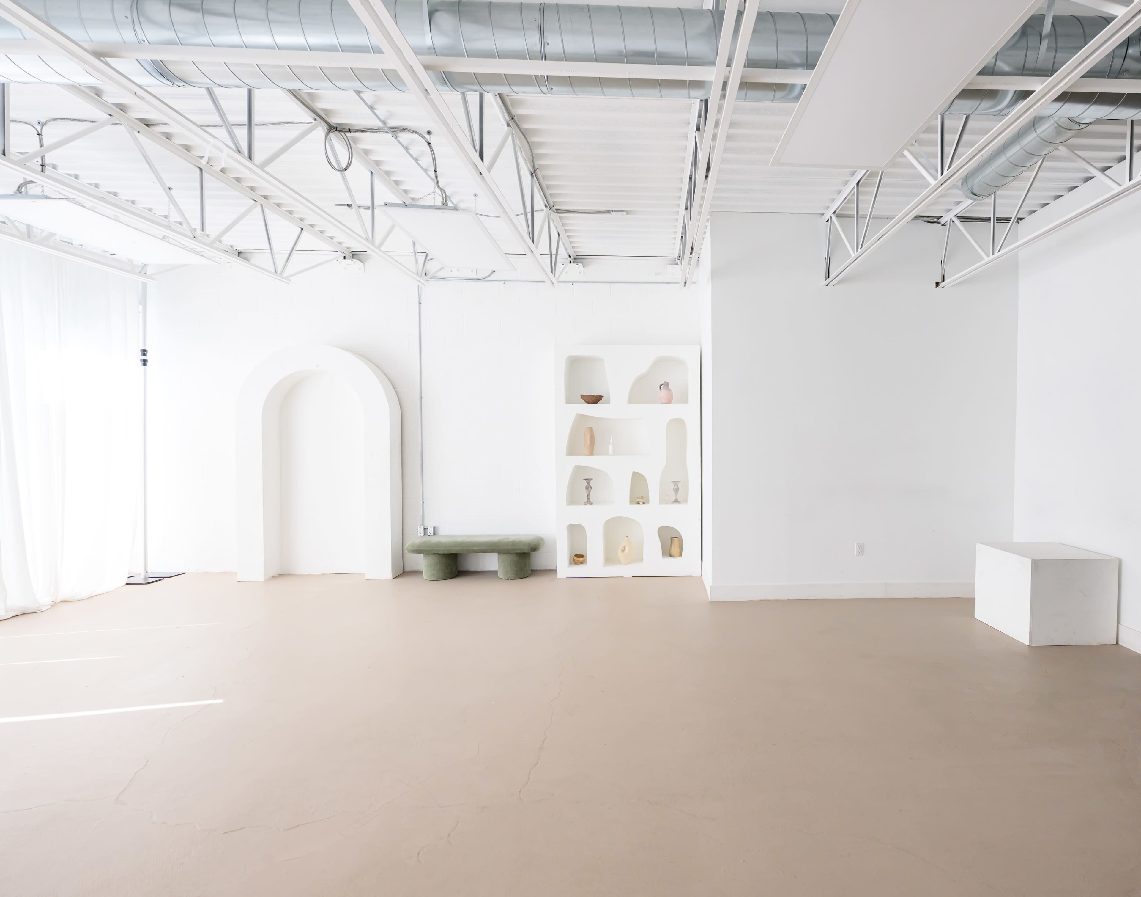 A spacious, minimalist interior features white walls, a light-colored floor, and simple shelving displaying decorative items.