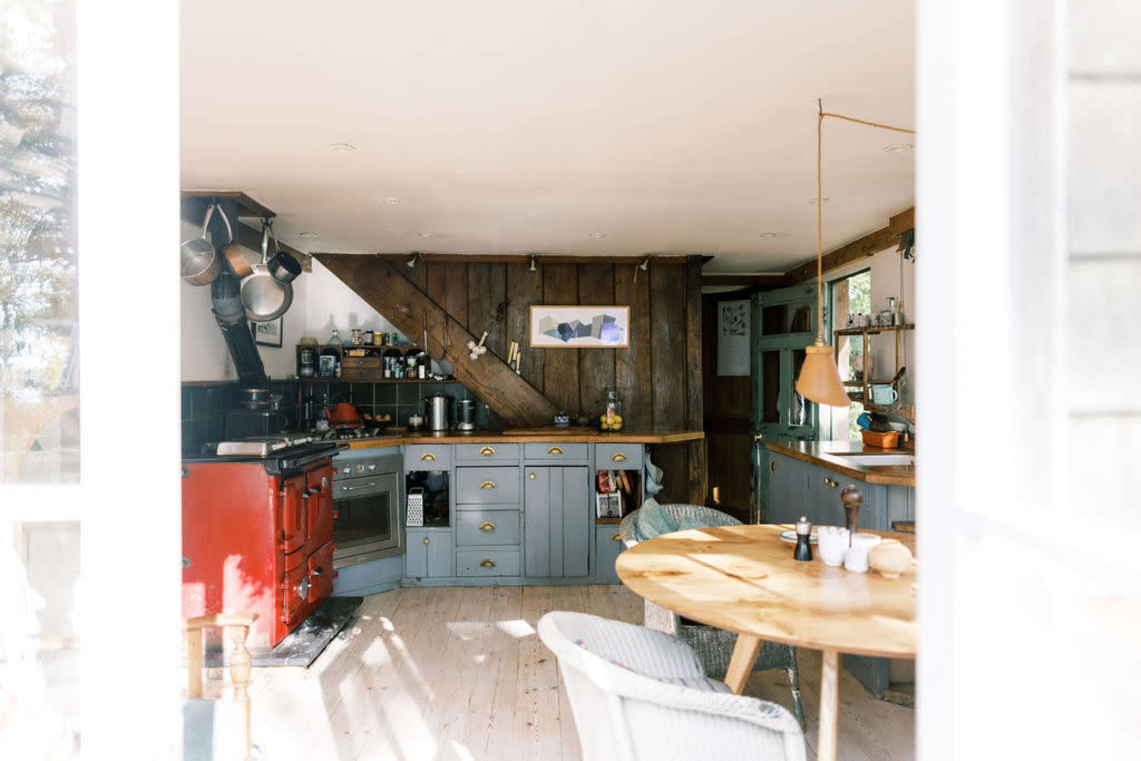 A cozy kitchen features a red stove, gray cabinetry, wooden accents, and a round dining table.
