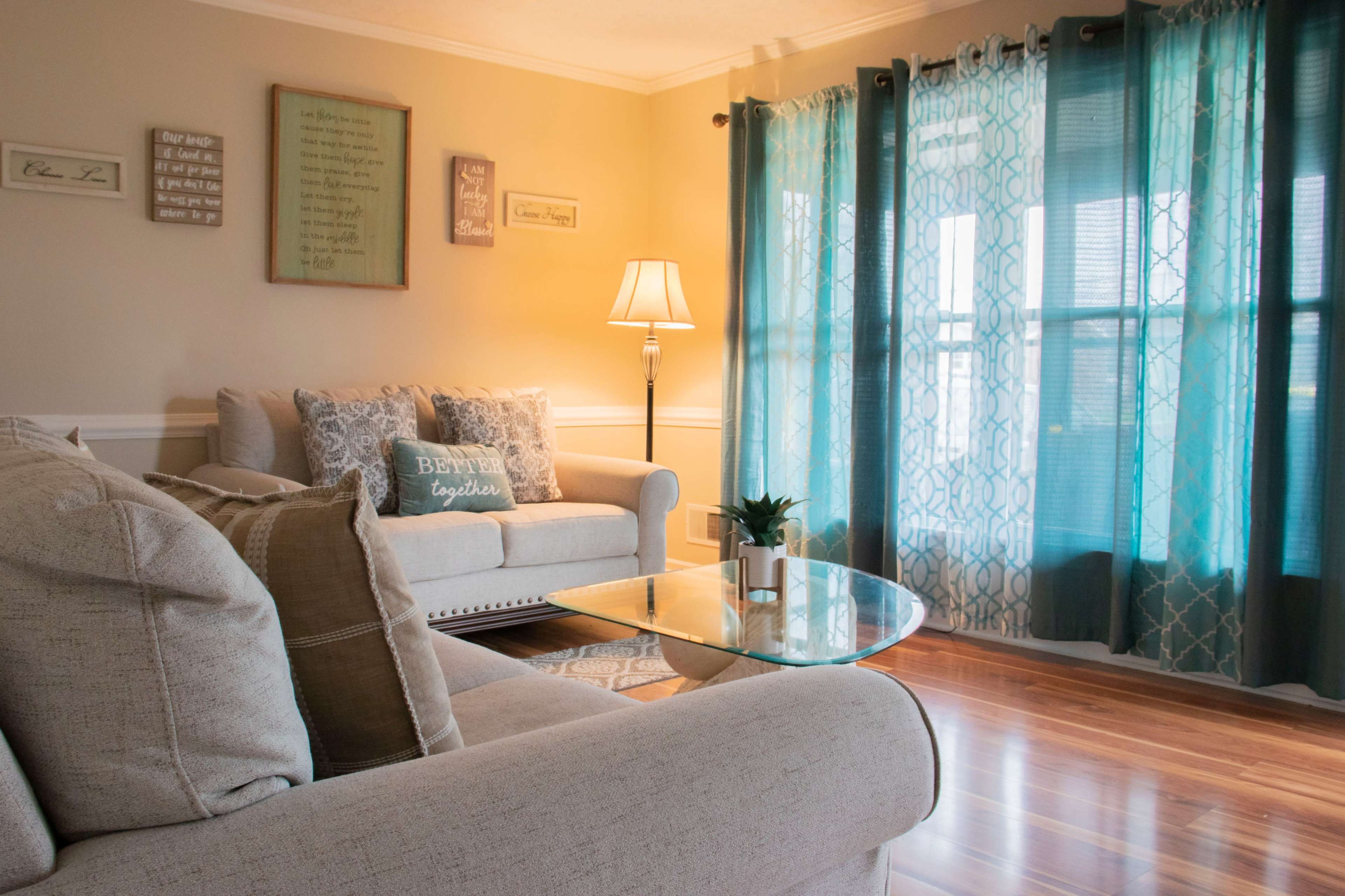 A cozy living room with two sofas, a glass coffee table, and large turquoise curtains letting light into the space.