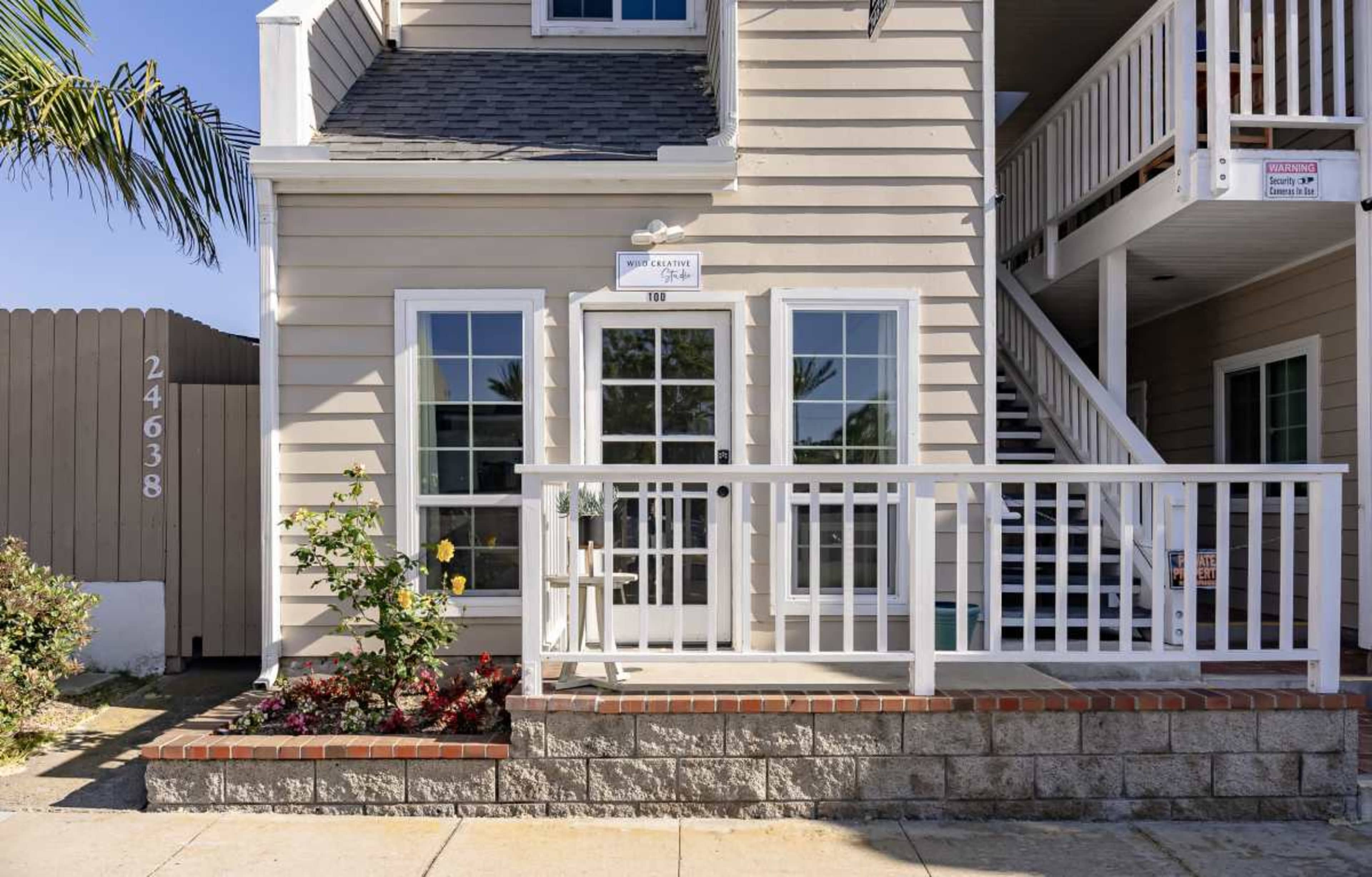 The image shows the entrance of a two-story building with a patio area, white railing, and a staircase leading to the second floor.