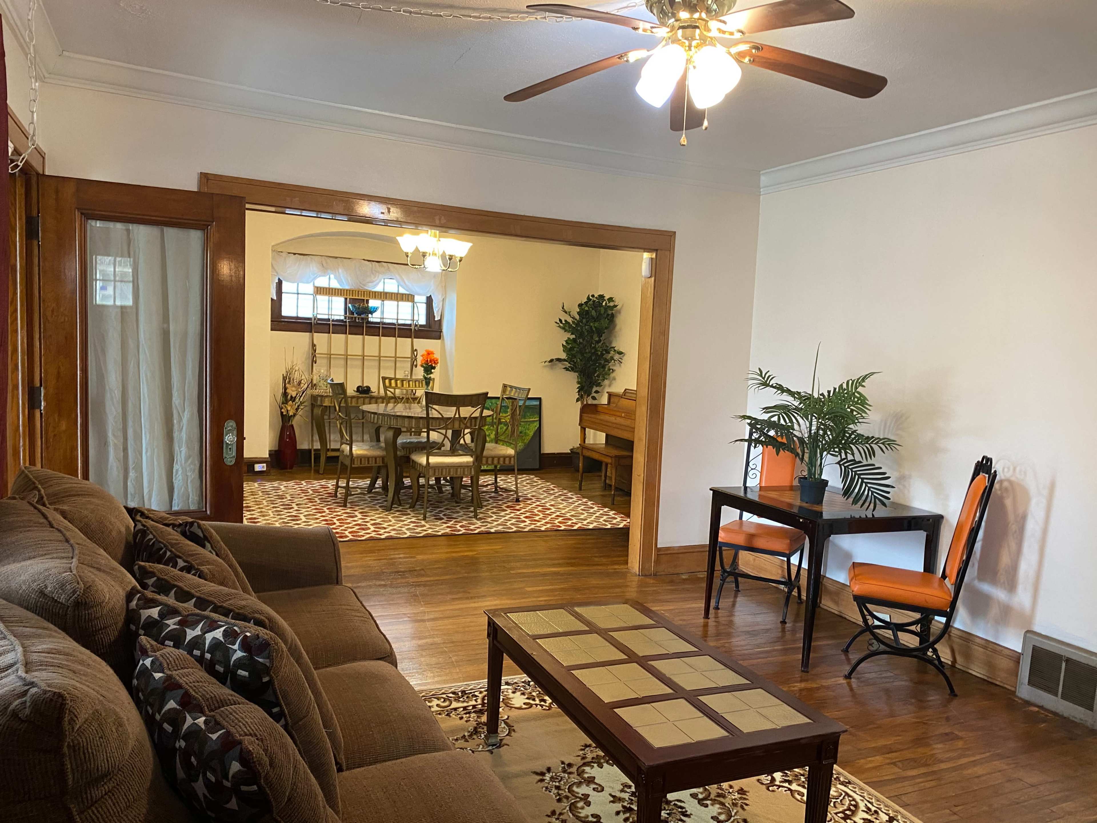 A living room furnished with a brown sofa, a coffee table, and a small dining area visible through an open doorway.
