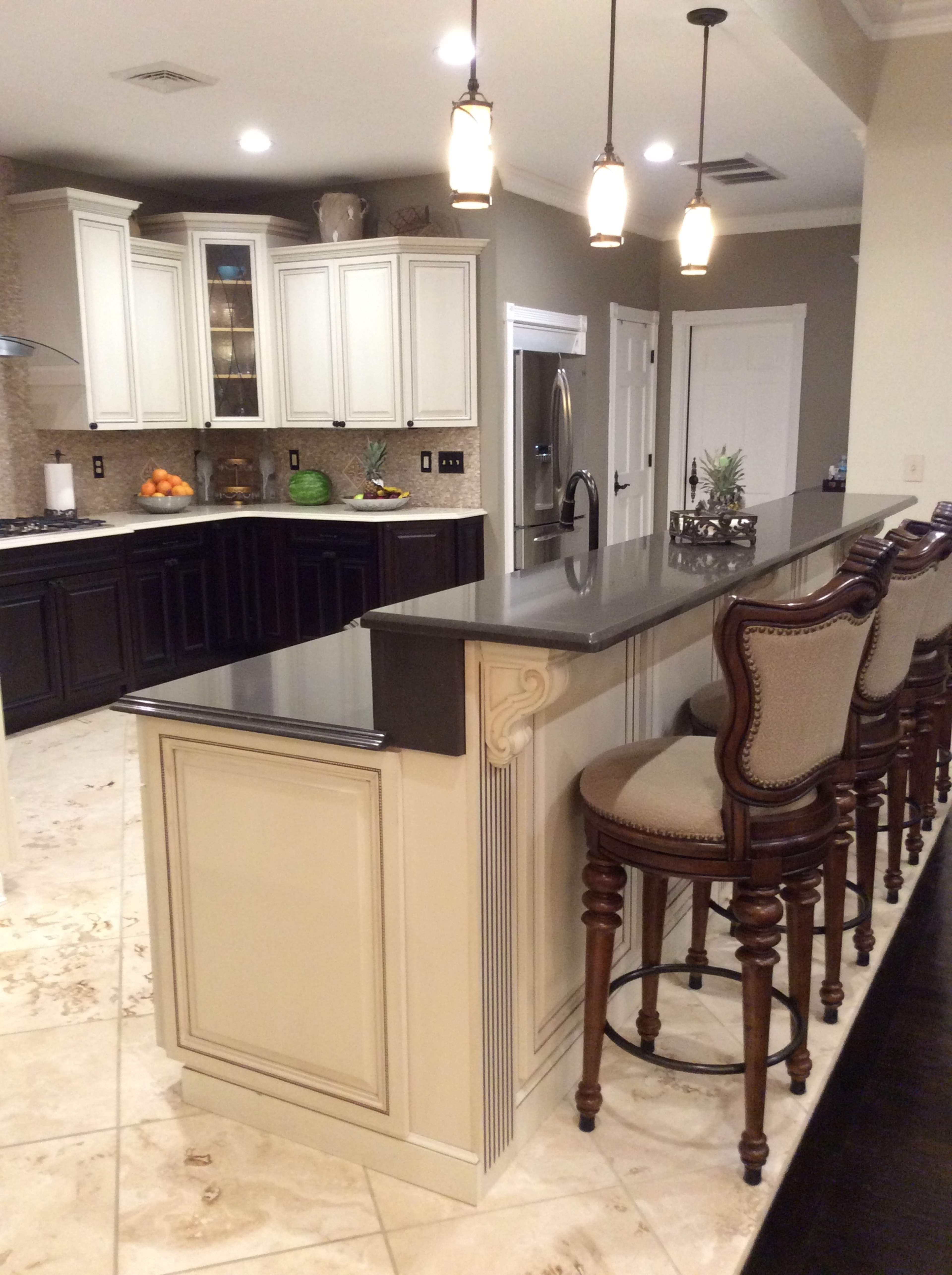 A kitchen featuring a large island with a dark countertop and several barstools, surrounded by cabinetry and appliances.