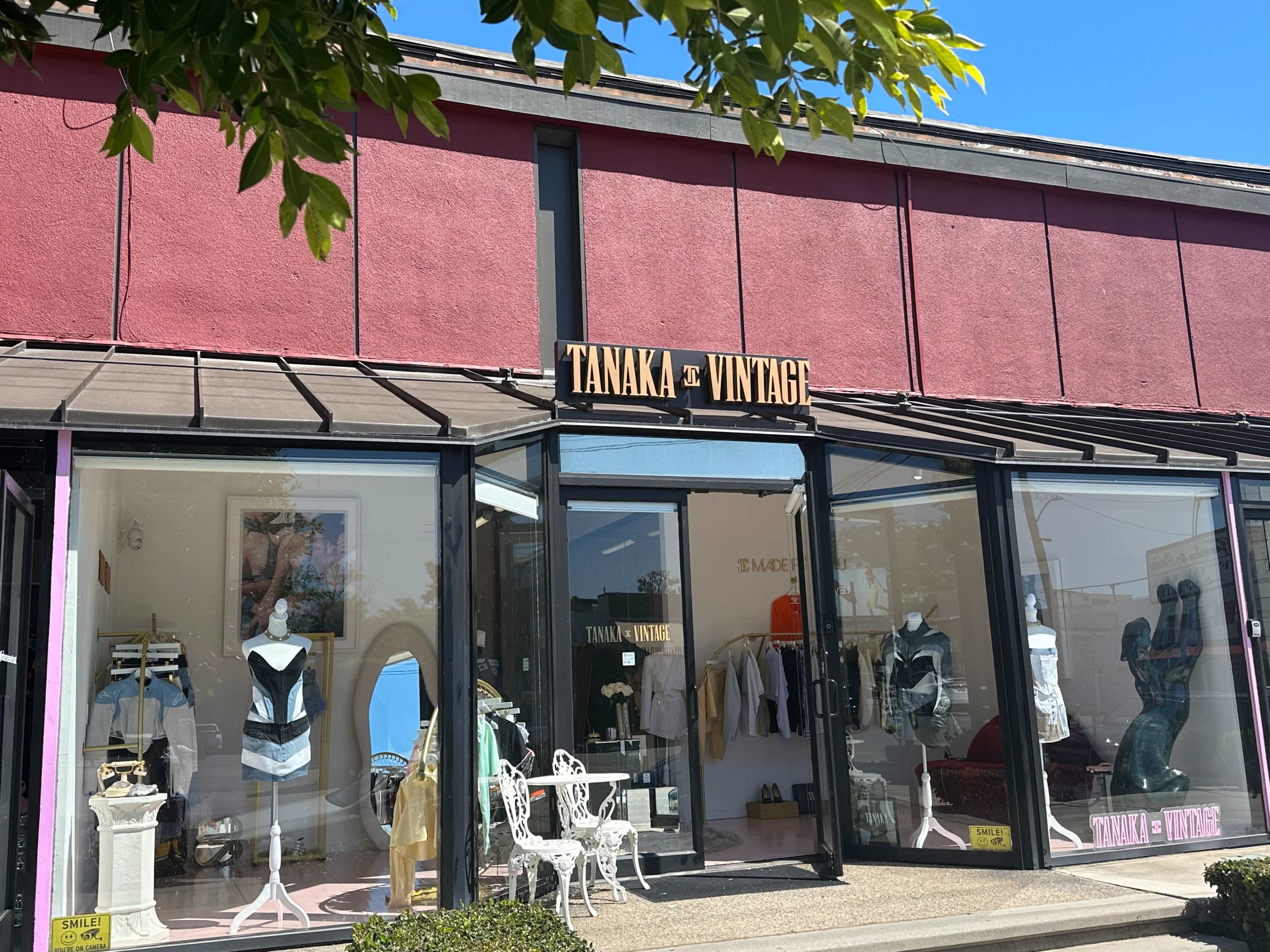 The storefront of Tanaka Vintage features large glass windows displaying vintage clothing and accessories, with outdoor seating in front.