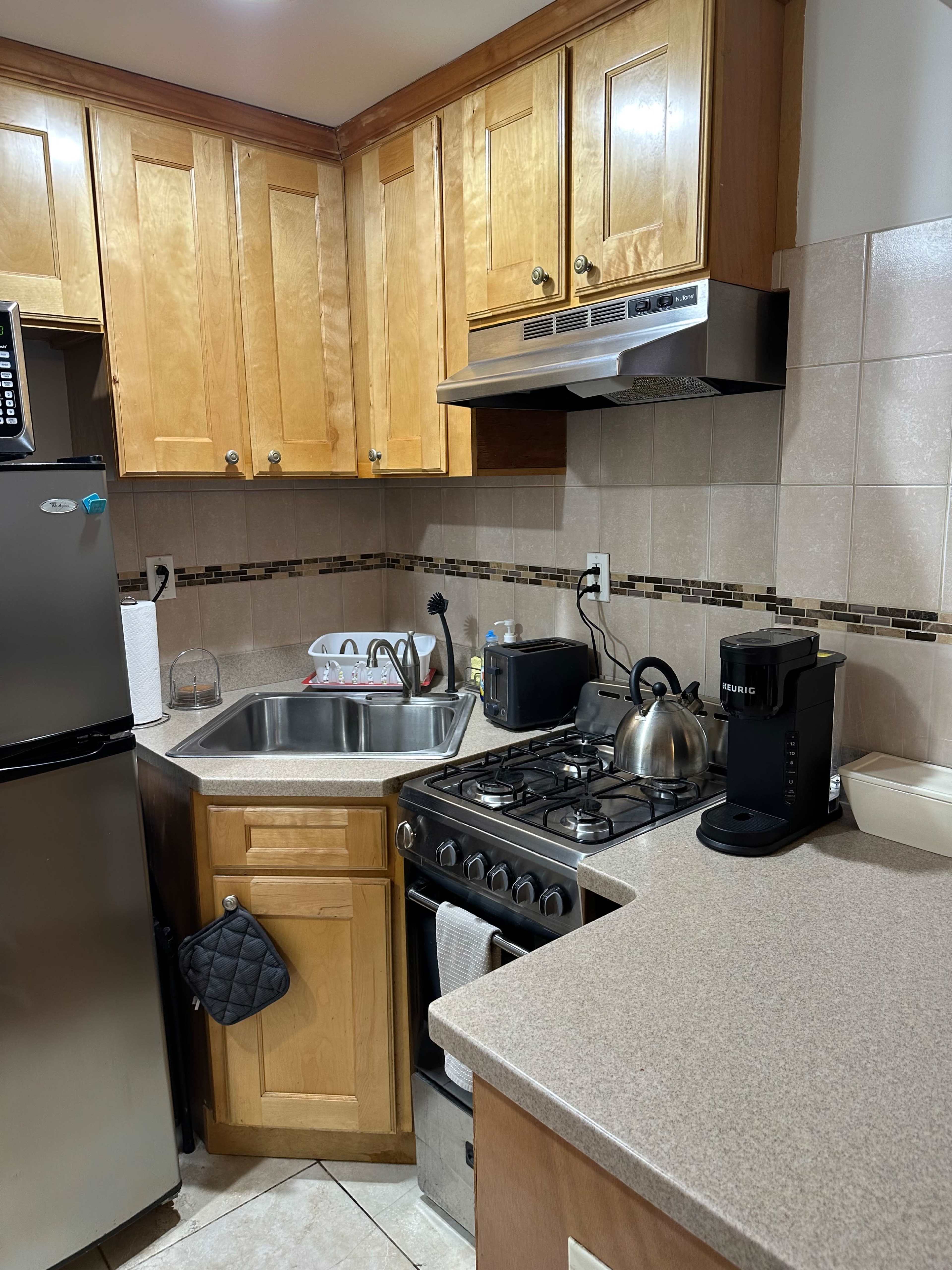 A compact kitchen features wooden cabinets, a stainless steel sink, a gas stove with an oven, and a coffee maker on the countertop.