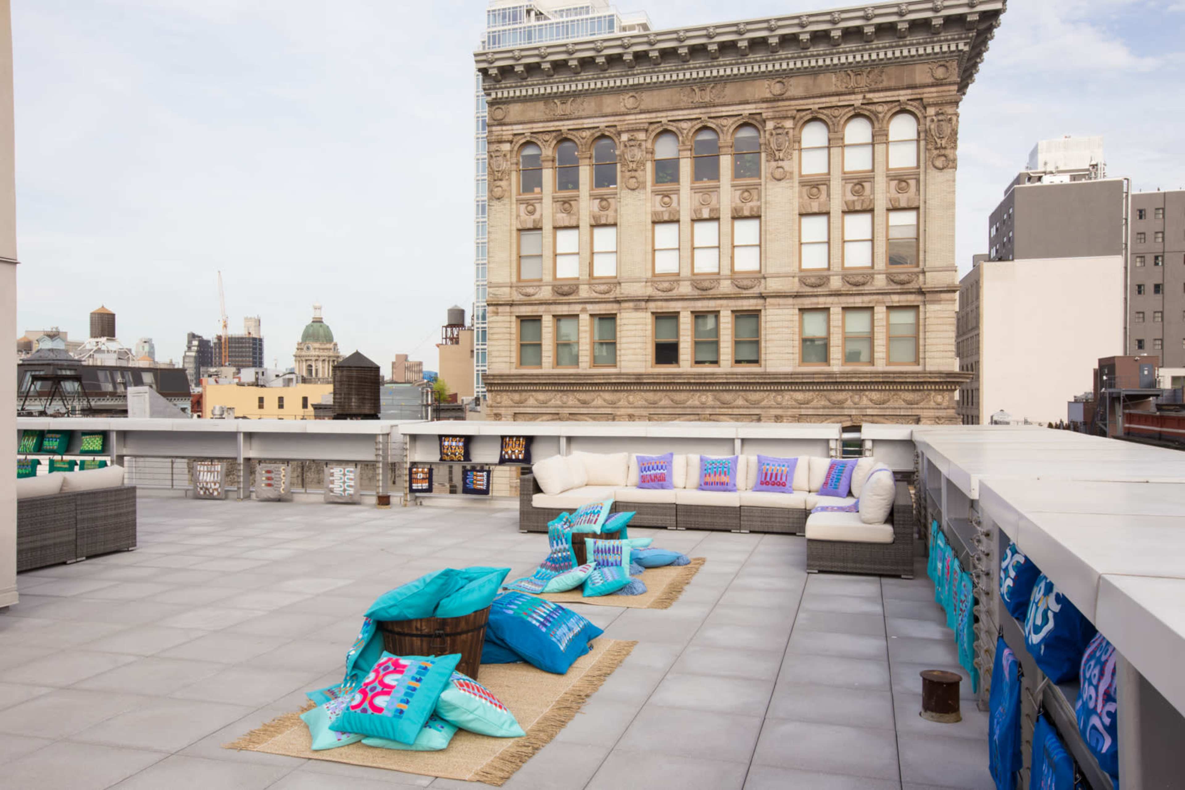 A rooftop terrace featuring modern furniture, colorful cushions, and a view of a historic building in the background.