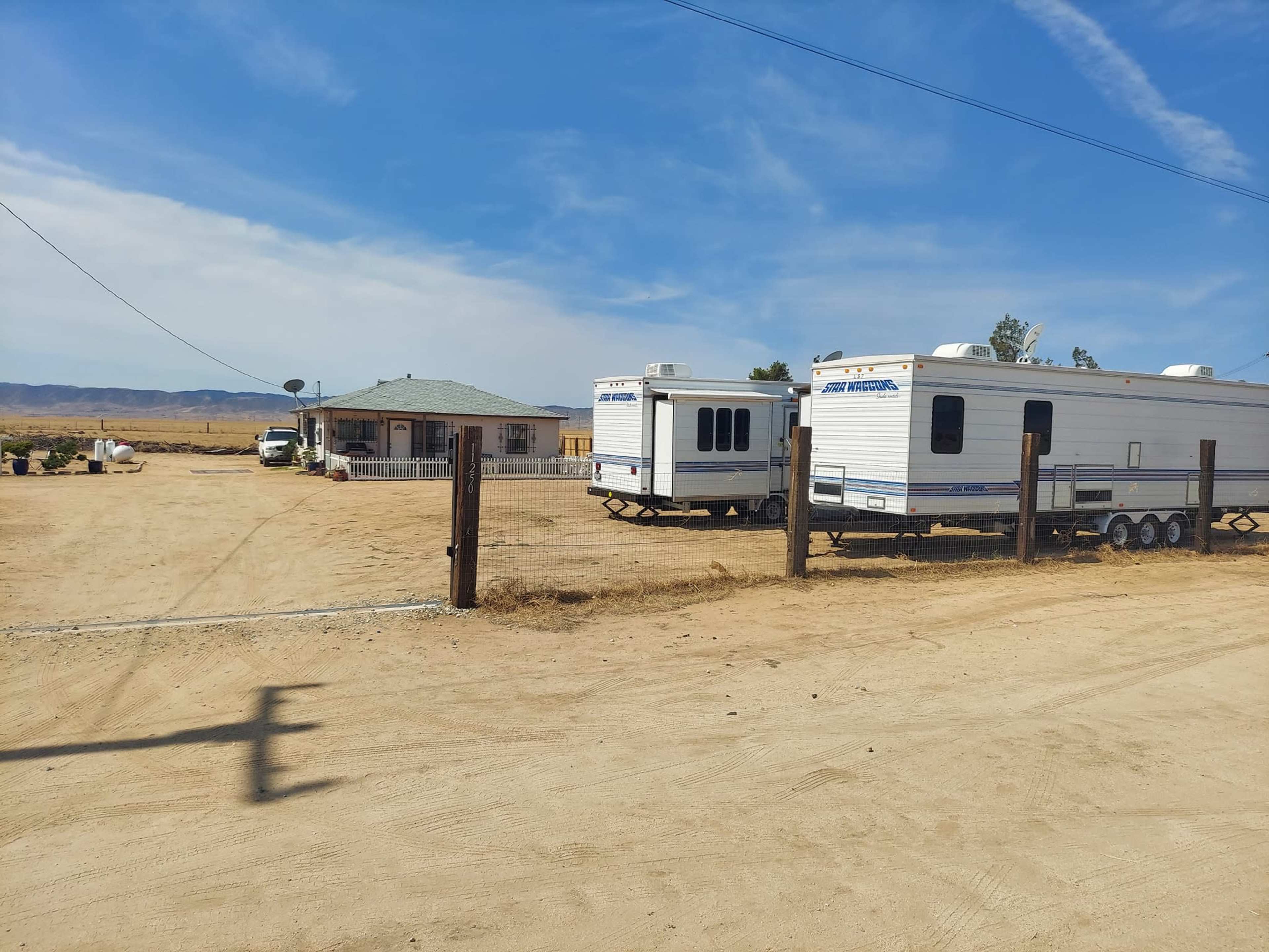 A single-story house with two trailers parked outside on a dirt road in a rural area.