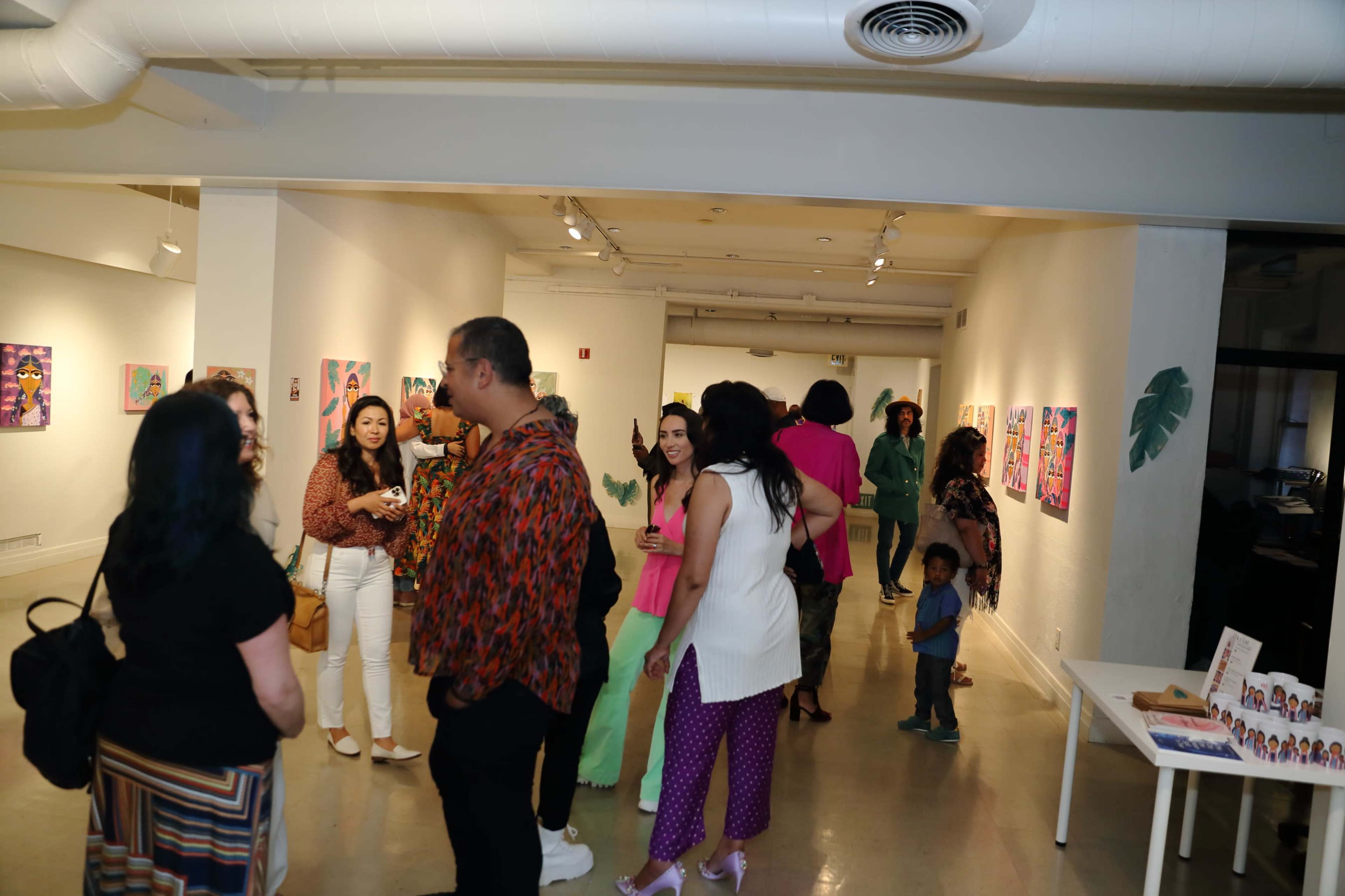 A diverse group of people socializes in an art gallery filled with colorful artwork on the walls.