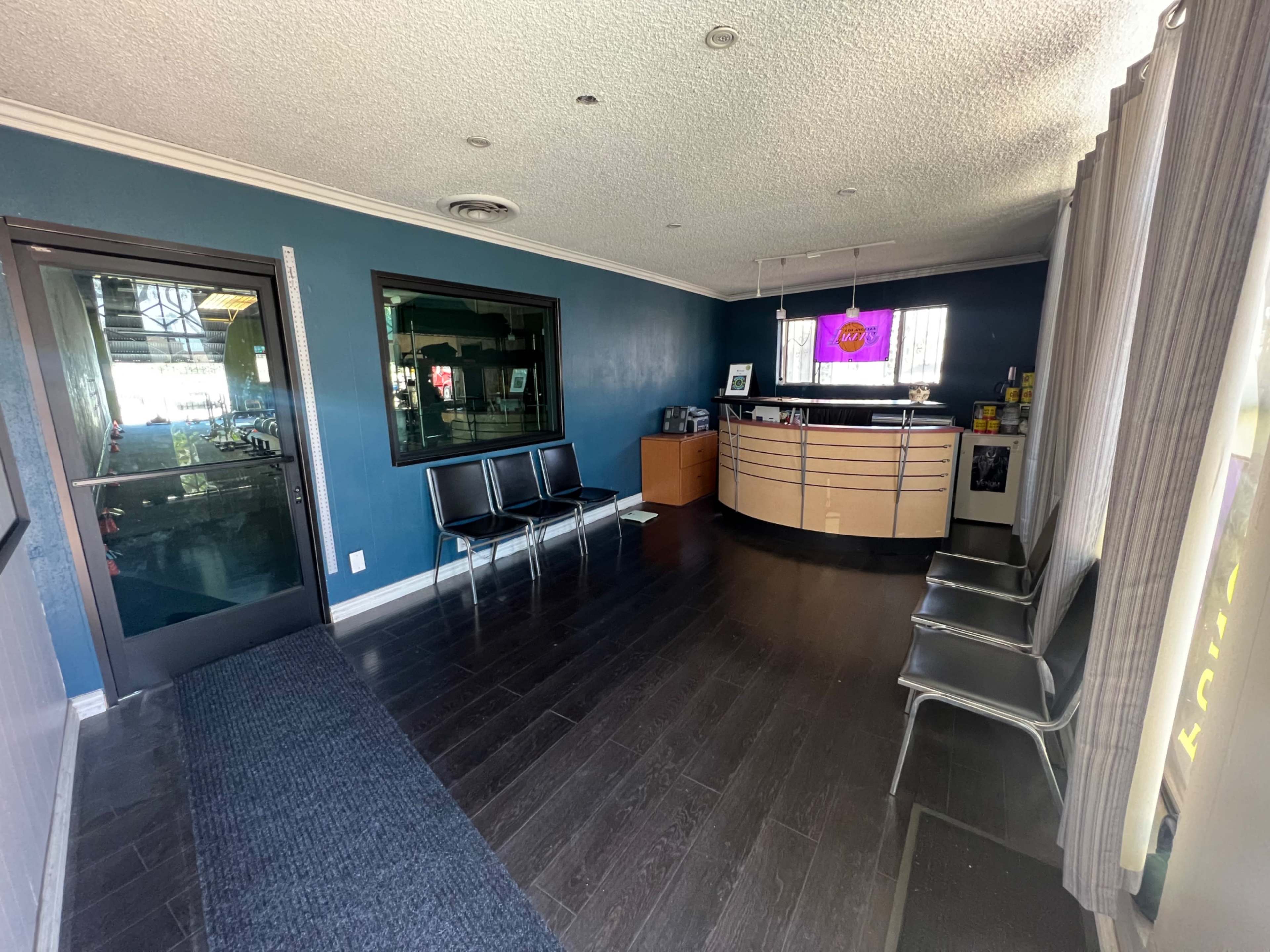 The image shows a waiting area with black chairs on one side and a reception desk on the opposite wall, featuring a large window and a colorful display.