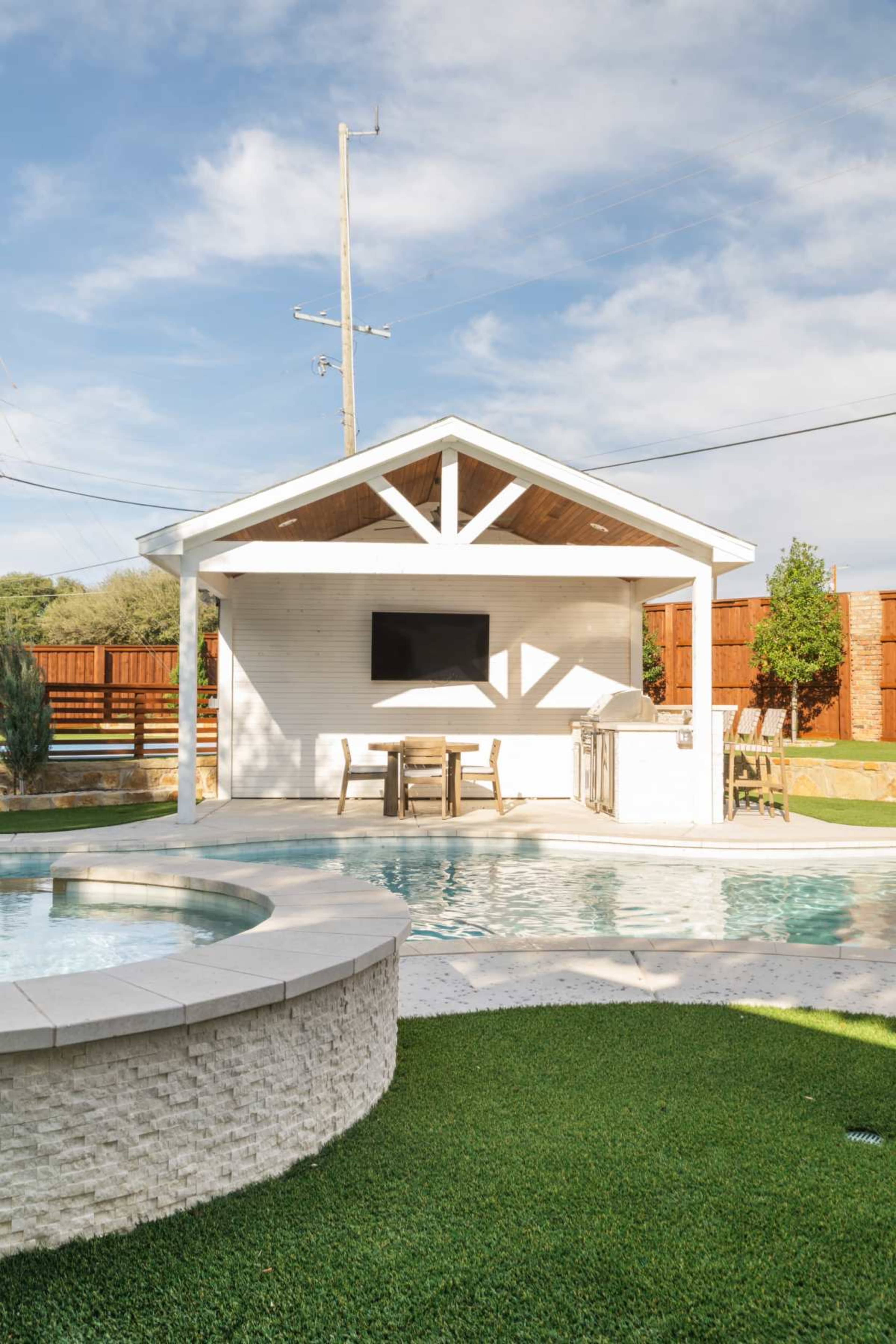 The image features a backyard with a poolside pavilion that includes a television and seating area, surrounded by a grassy lawn and a swimming pool.