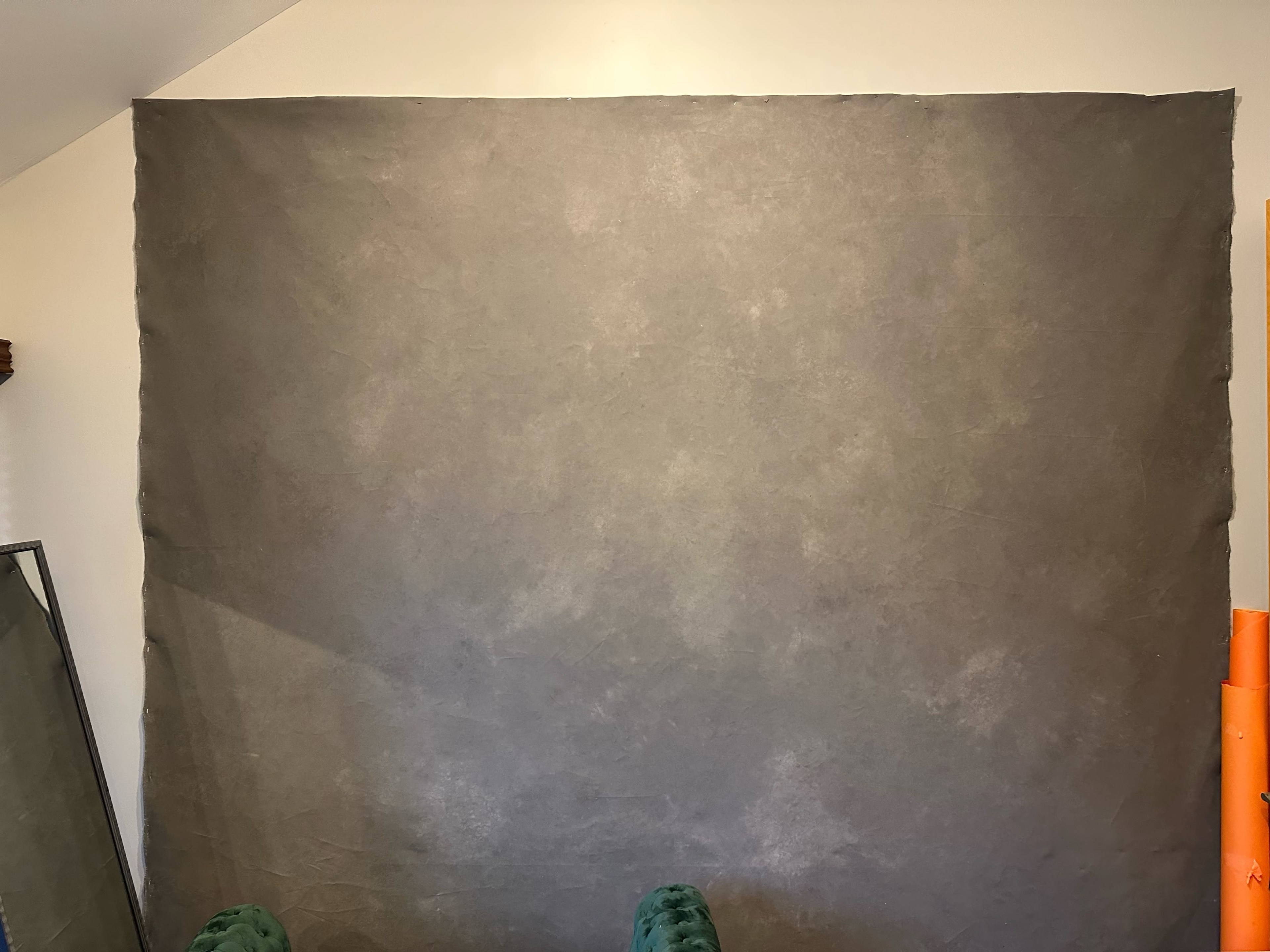 The image shows a blank, textured gray backdrop with a few rolls of orange material and a mirror on the left side.