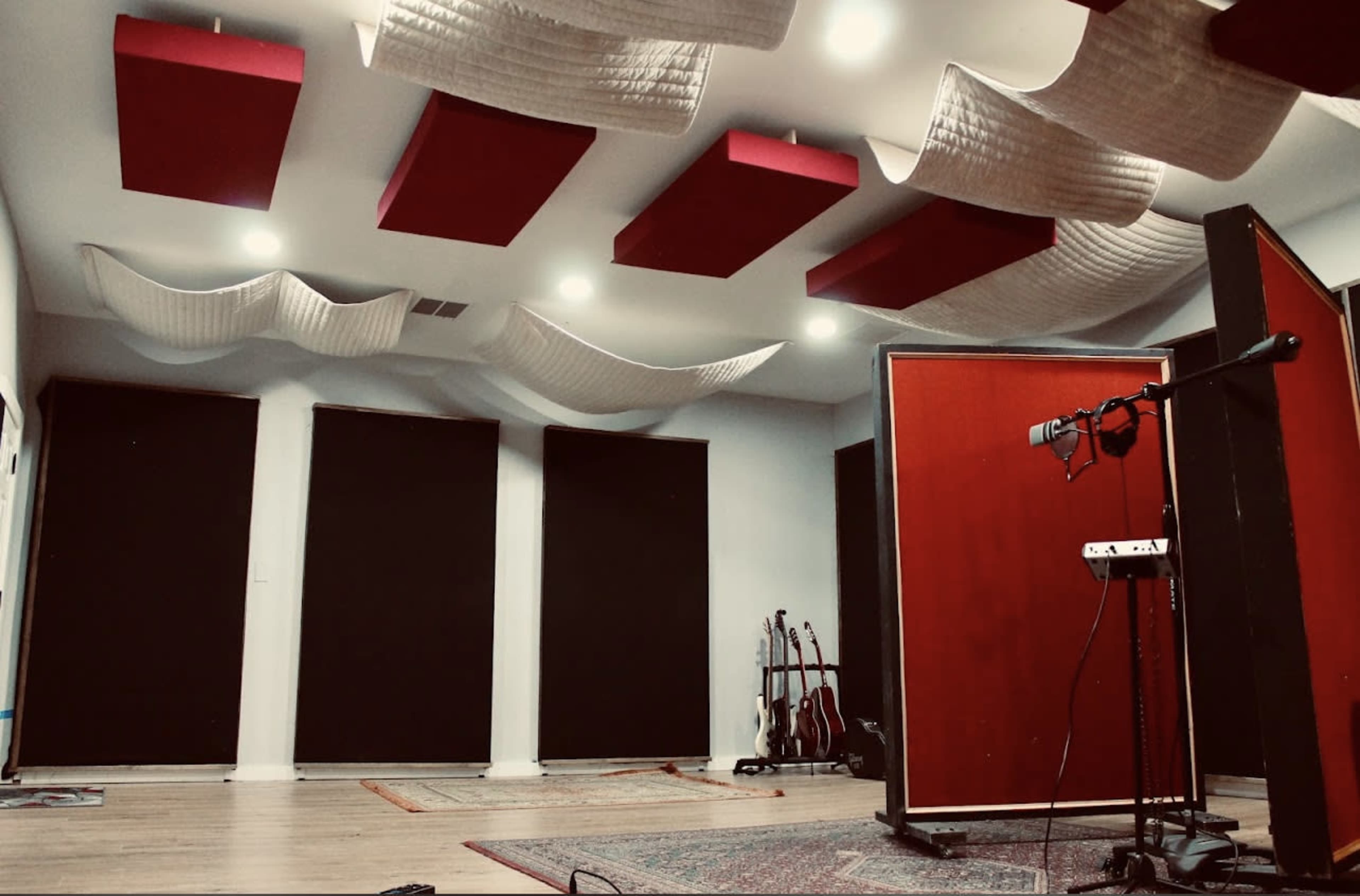A soundproof recording studio features red acoustic panels on the ceiling, black soundproofing curtains on the windows, and various musical instruments against the wall.