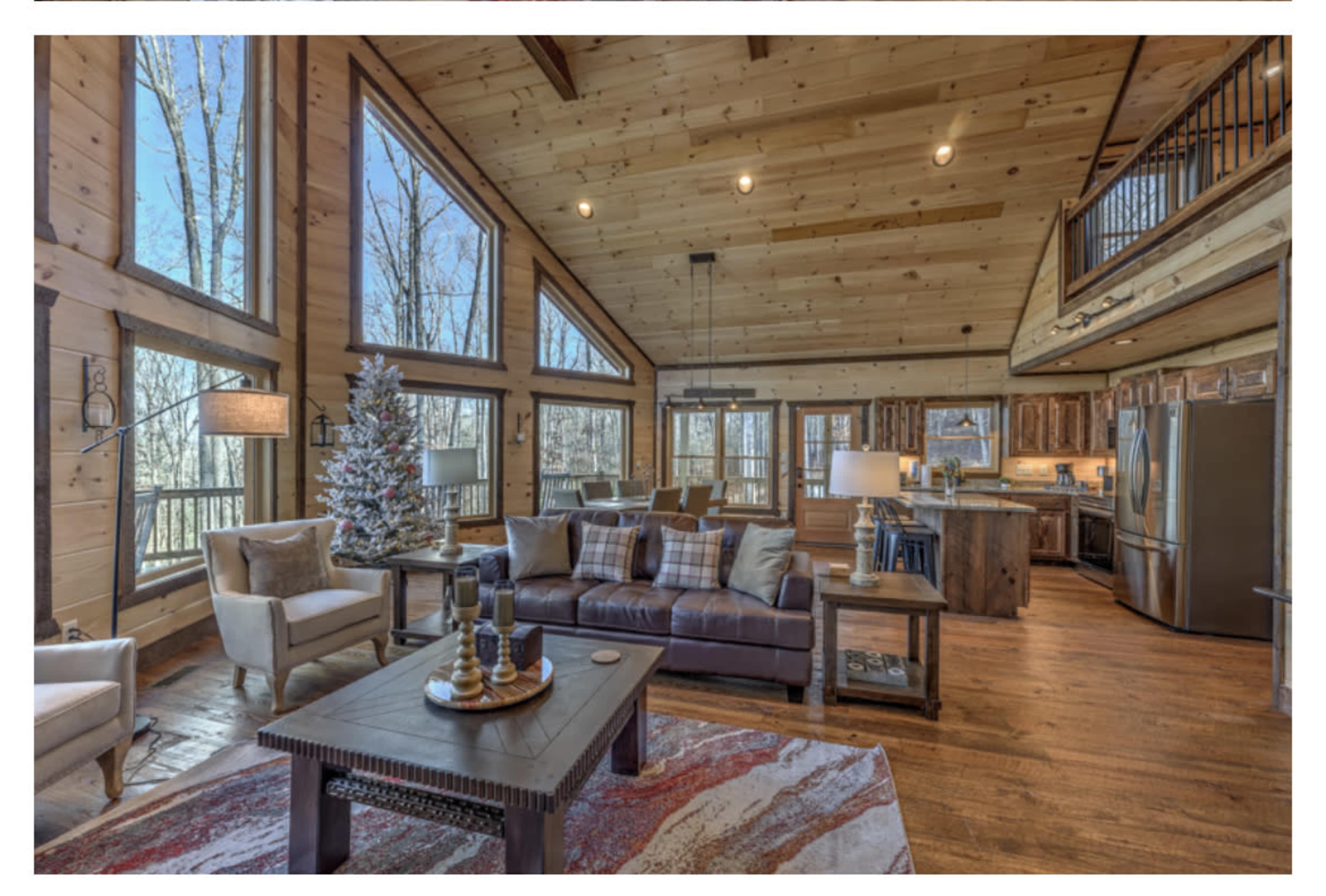 A modern wooden interior features a spacious living area with large windows, a cozy seating arrangement, and a view of the outside trees.