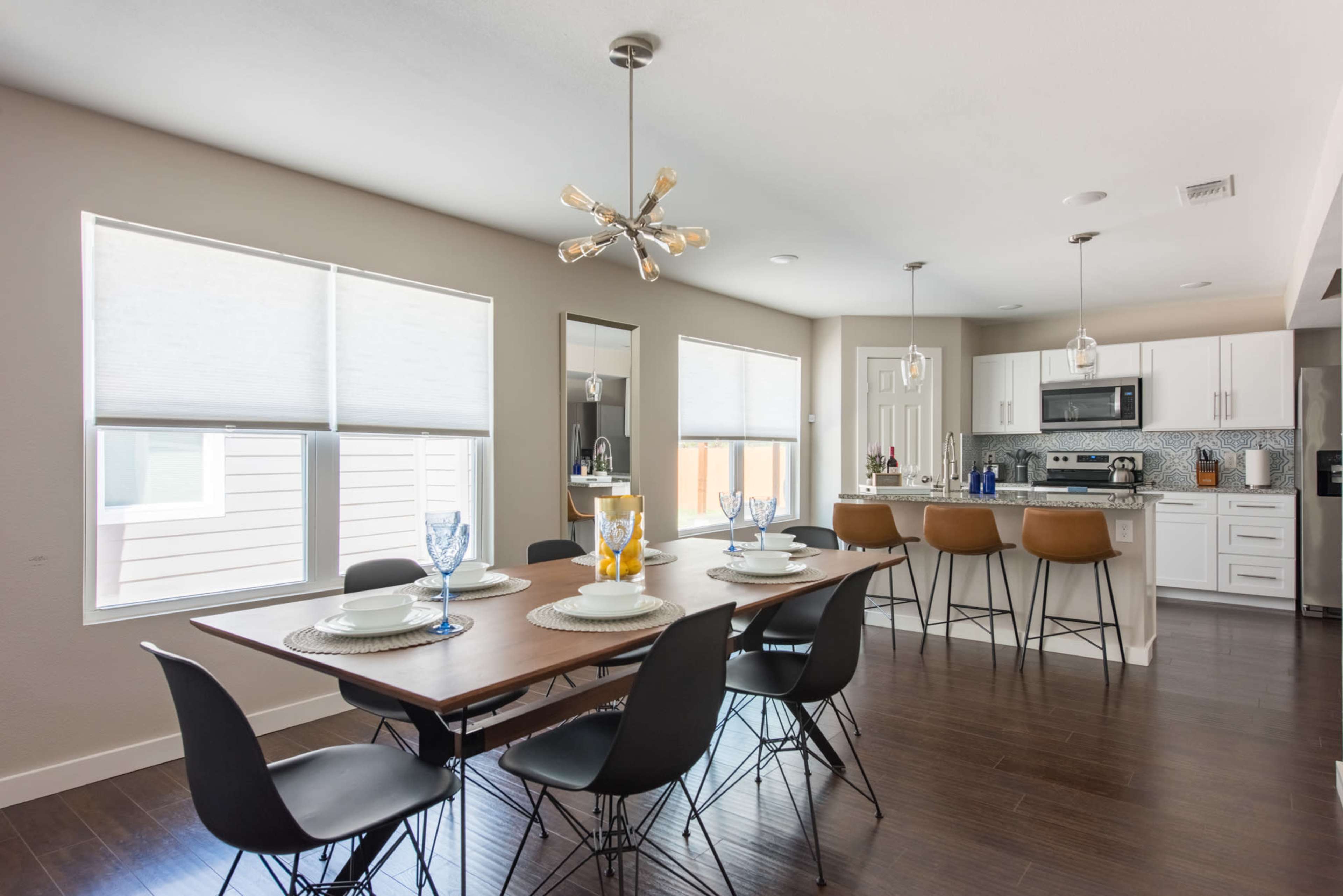 A dining area features a wooden table set for six and leads into a modern kitchen with bar seating and stainless steel appliances.