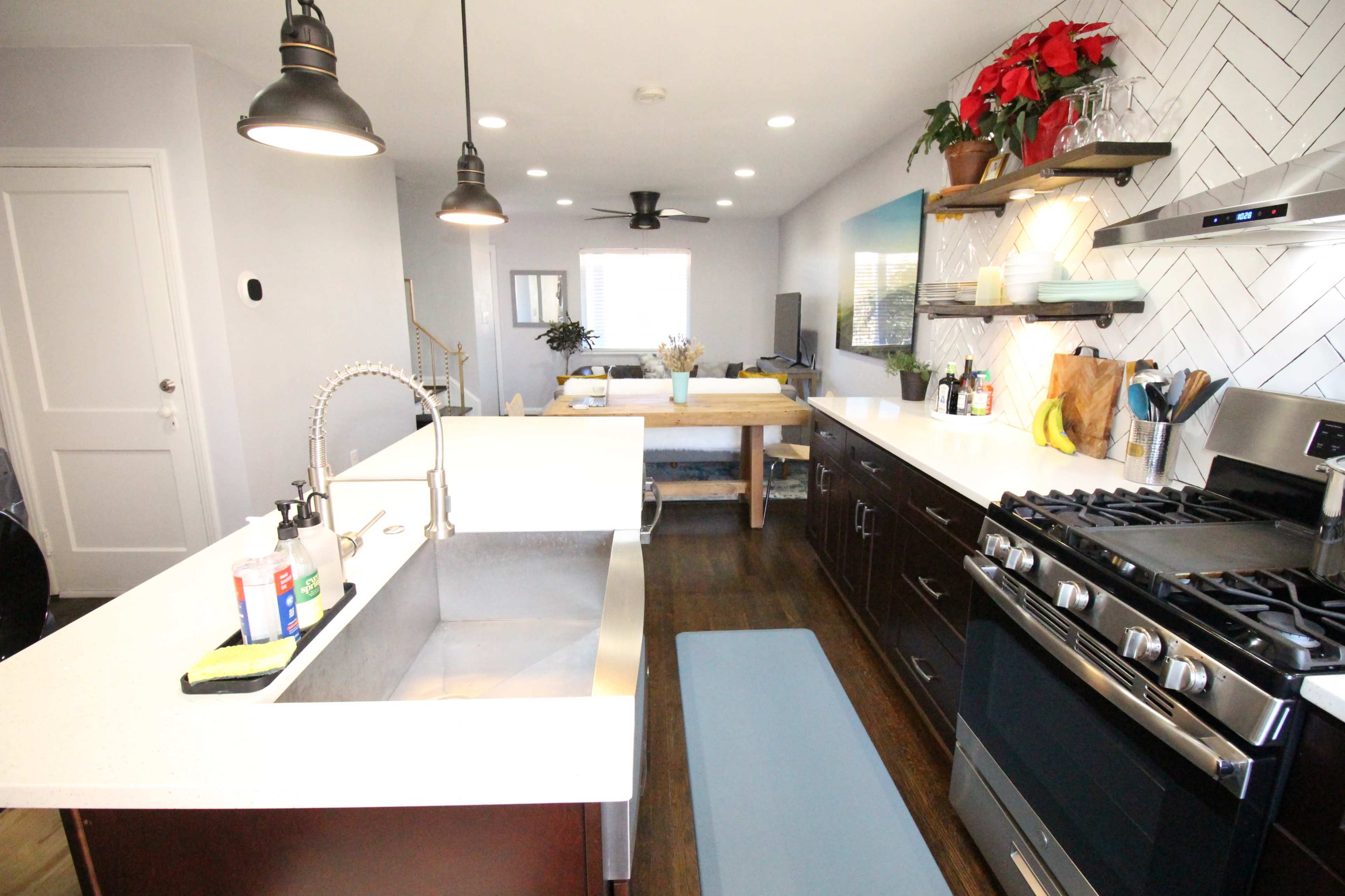 A modern kitchen features a stainless steel sink, dark wooden cabinets, and a gas stove, with a dining area visible in the background.