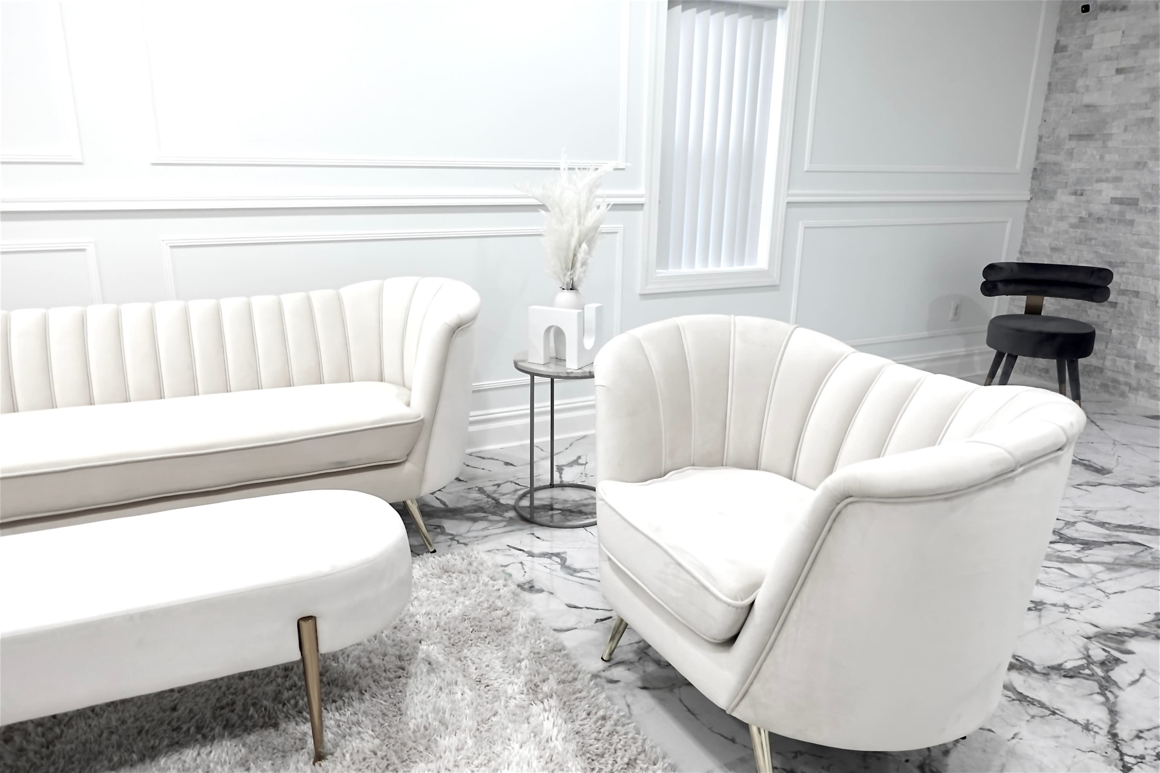 A modern living room setup featuring a white velvet sofa and armchair with gold legs, a round side table, and marble flooring.