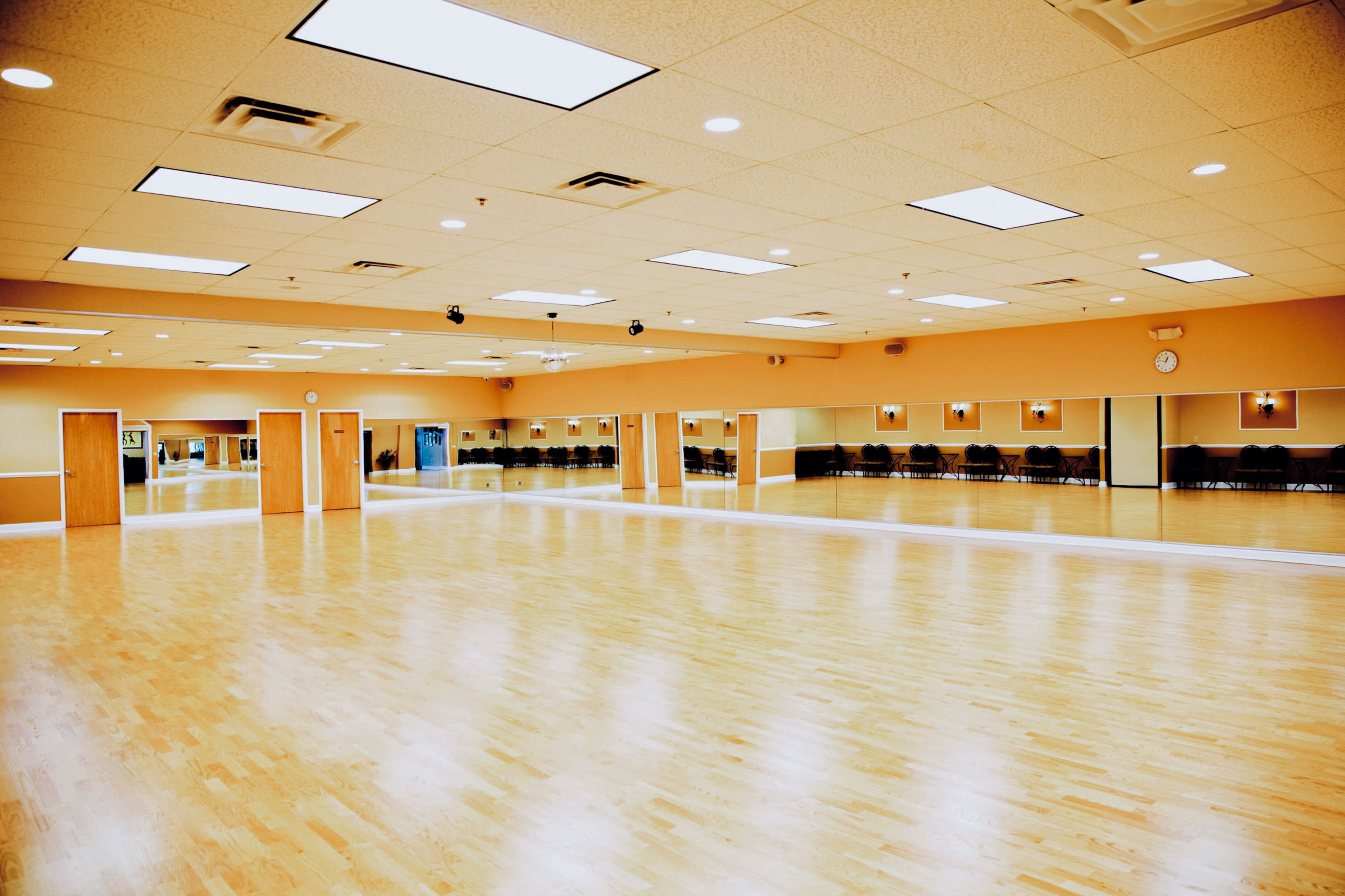 A spacious, well-lit dance studio with a wooden floor and mirrors along the walls.