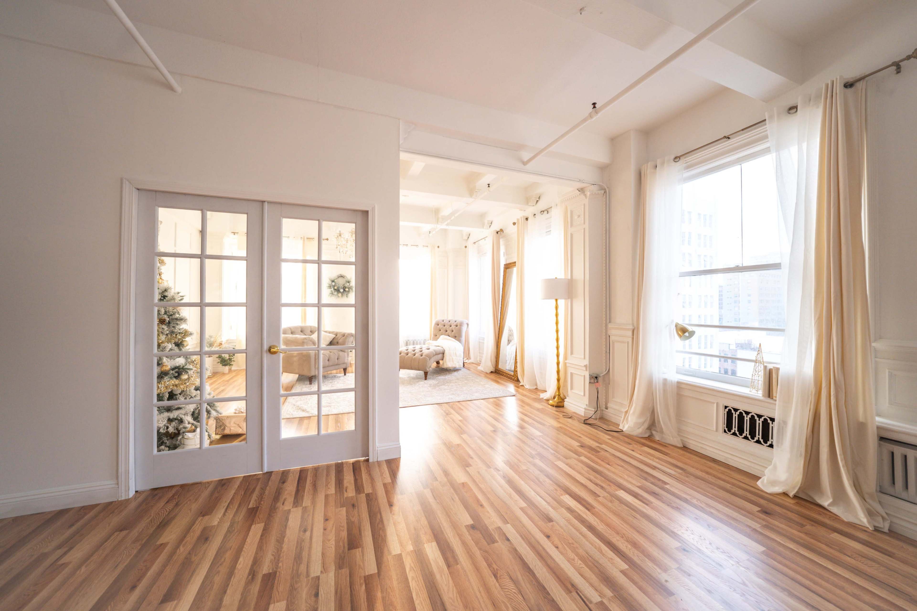 A bright, open living space with hardwood floors, large windows, and a glass-paned door leading to a cozy seating area.