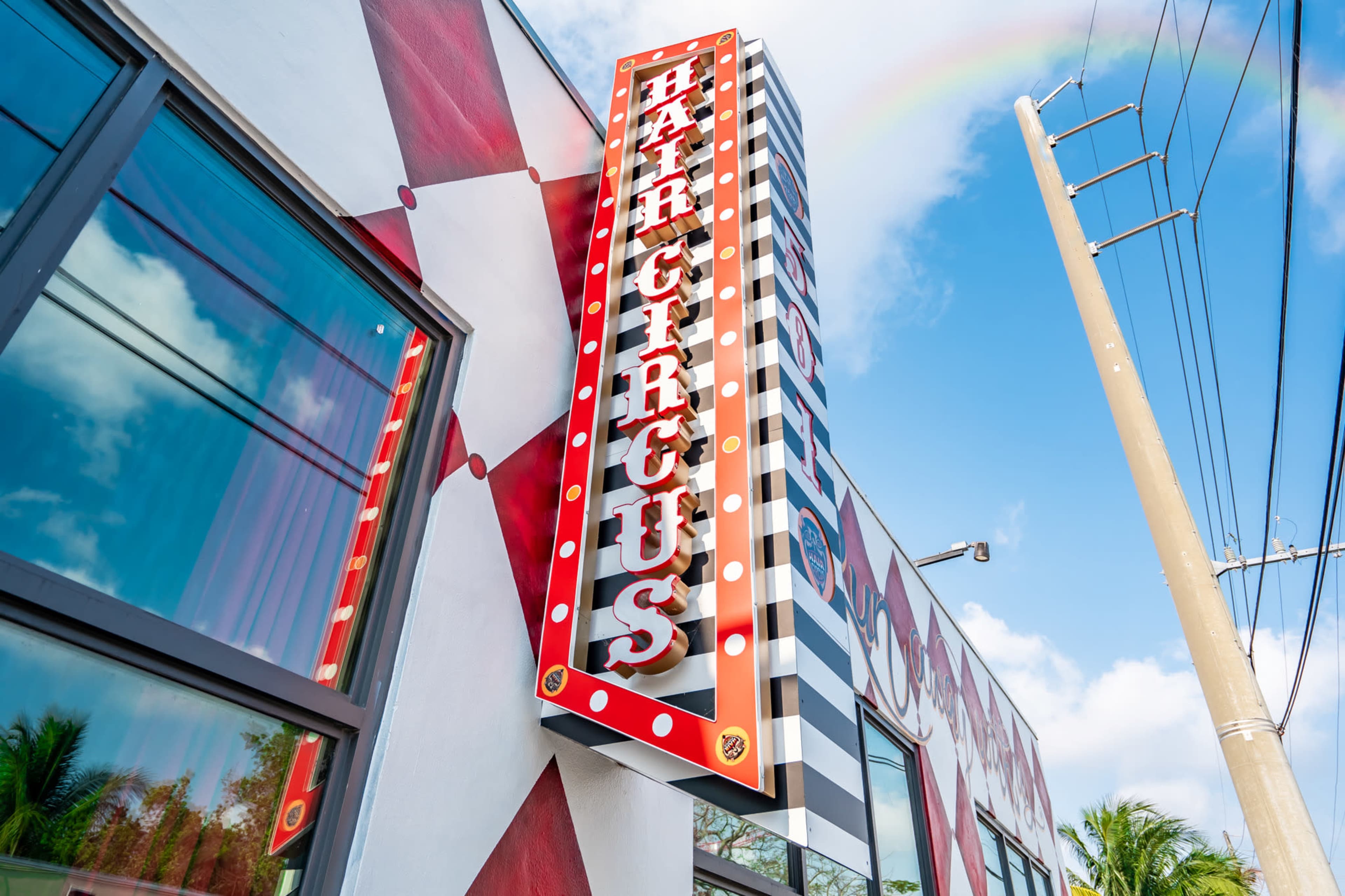 A brightly colored building features a large illuminated sign that reads "HAIR CIRCUS" with a rainbow in the background.