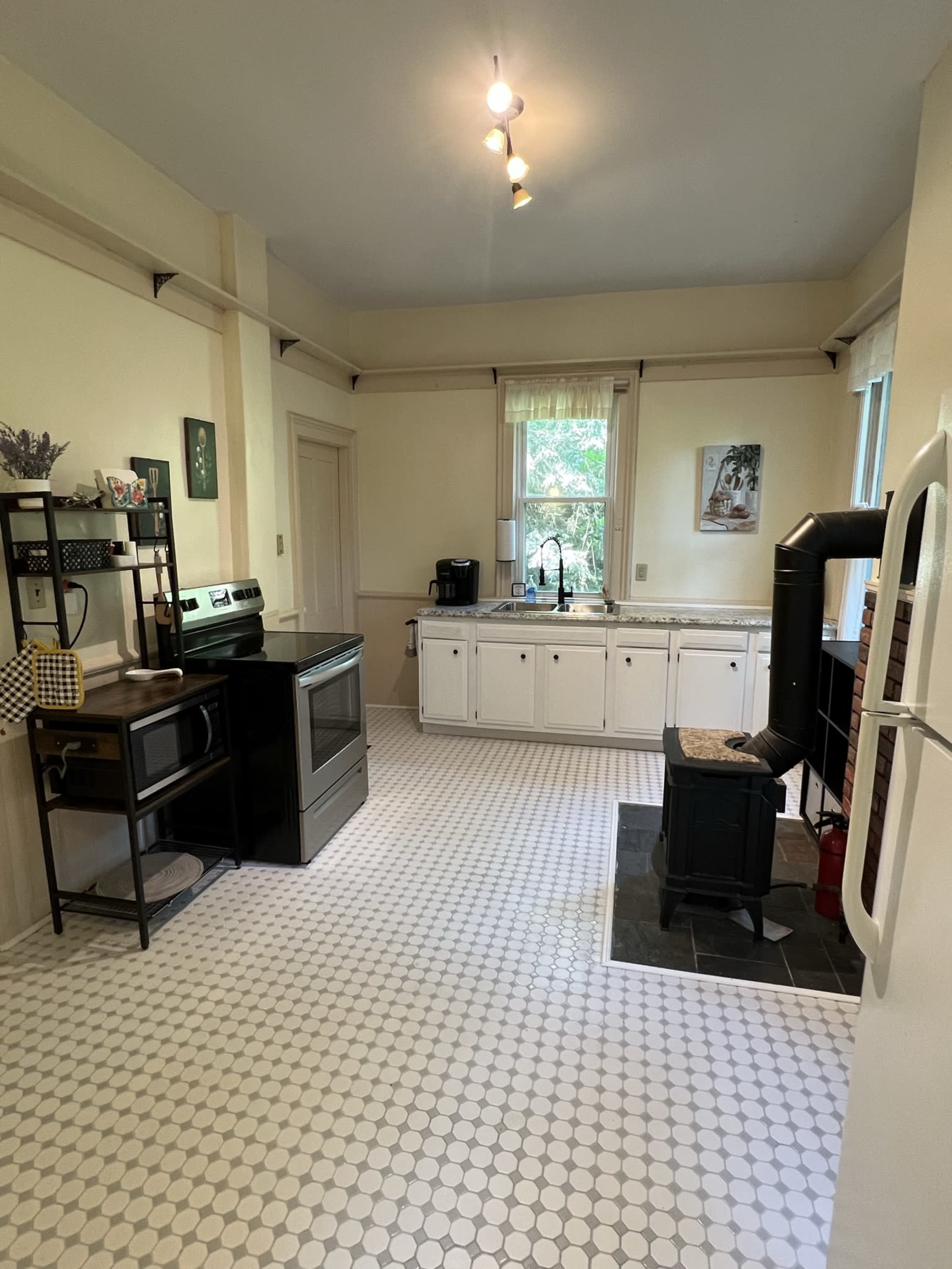 A spacious kitchen featuring a black stove, white cabinets, and a tiled floor with a vintage feel.