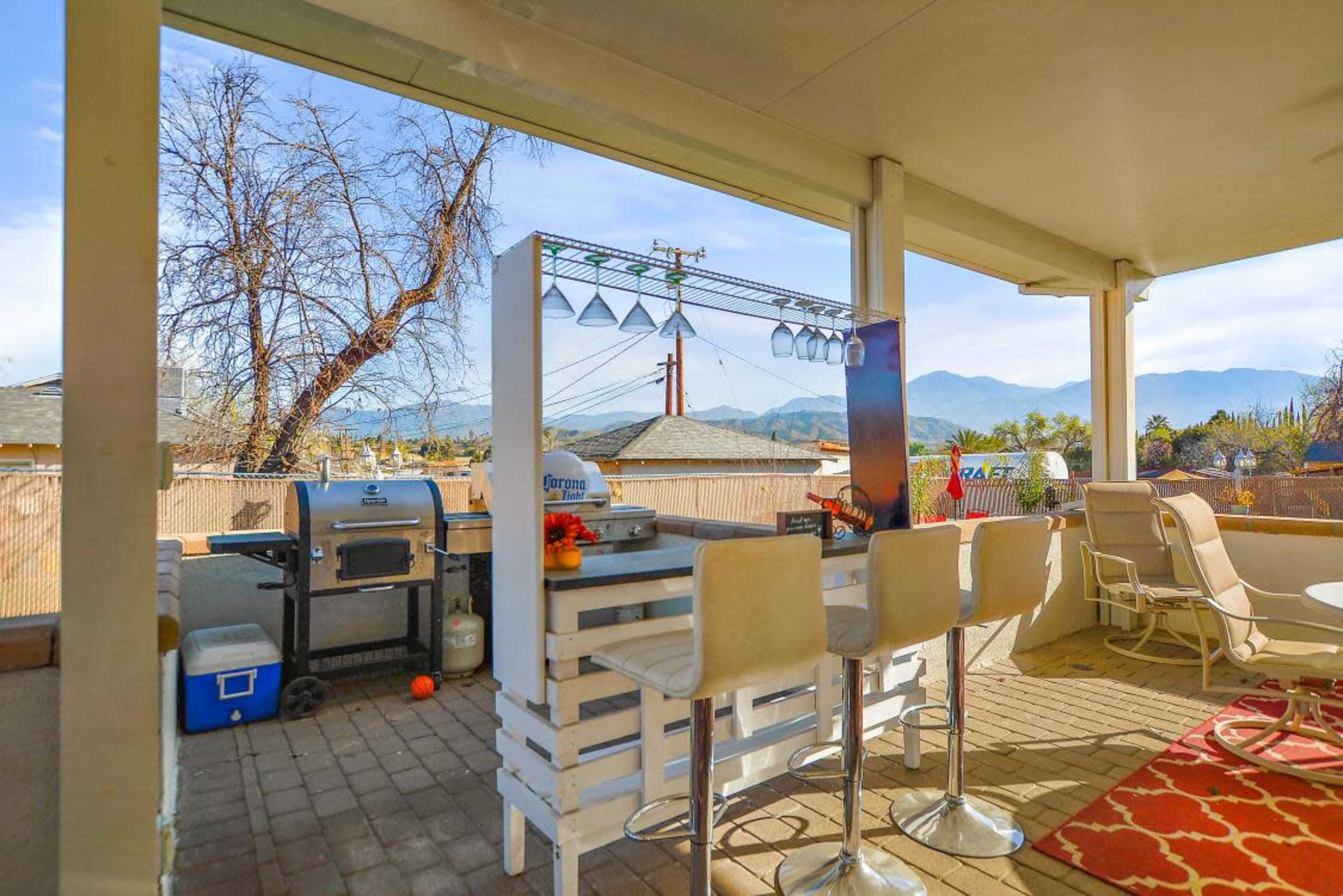 A covered outdoor patio with a bar area, grill, and views of mountains in the distance.