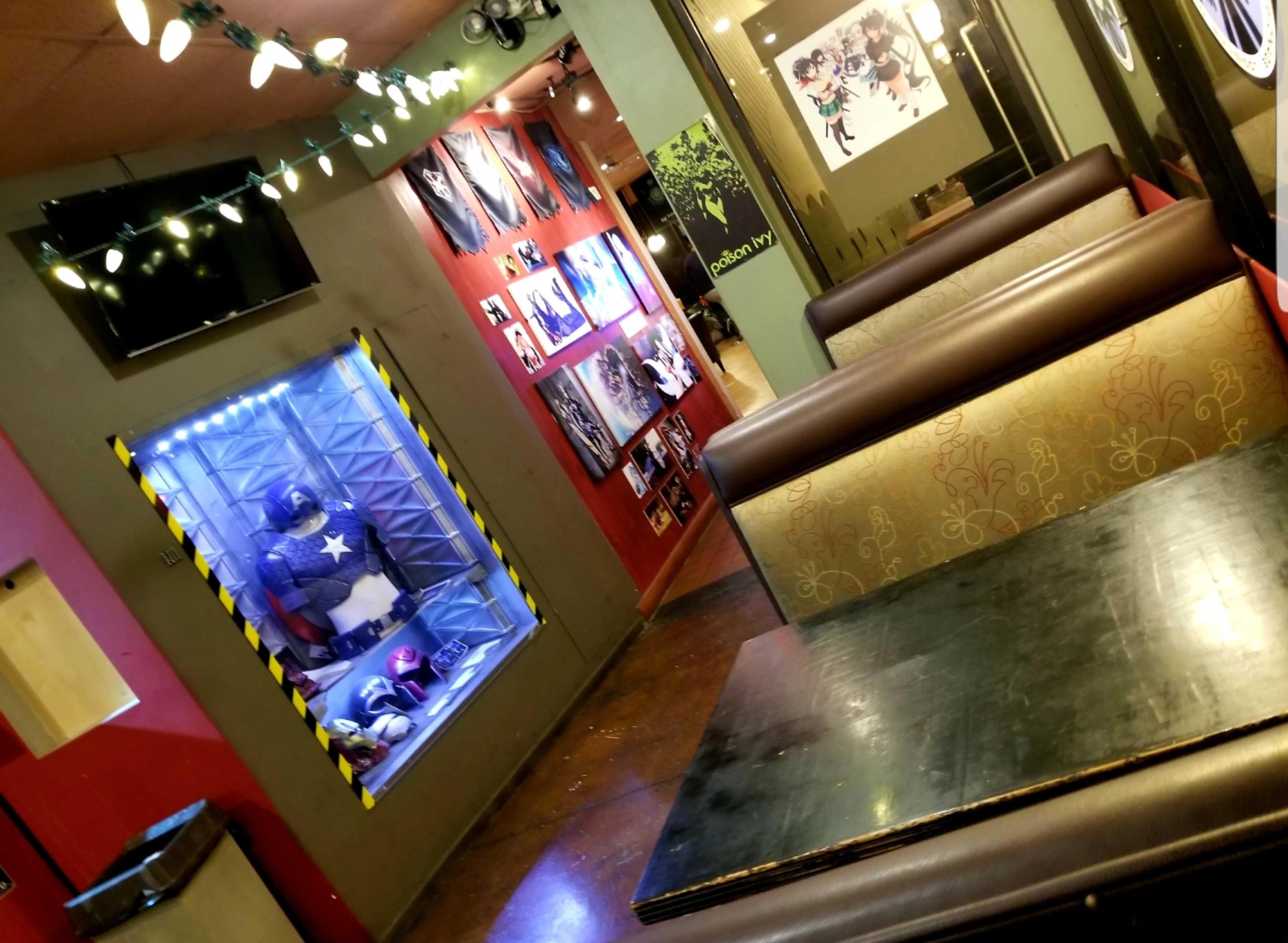 The image shows a spacious interior of a themed restaurant, featuring booth seating and walls adorned with various framed pictures and a display case with a superhero figure.