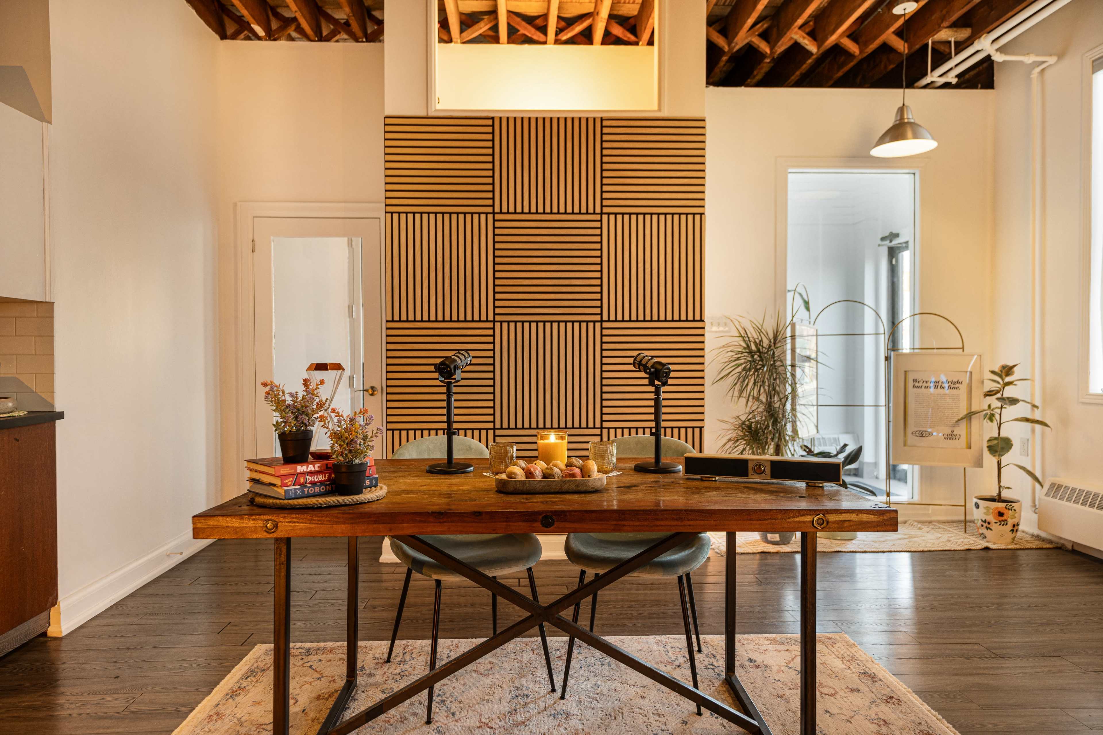 A well-lit office space features a wooden table with two chairs, decorative items, and a patterned wall in the background.