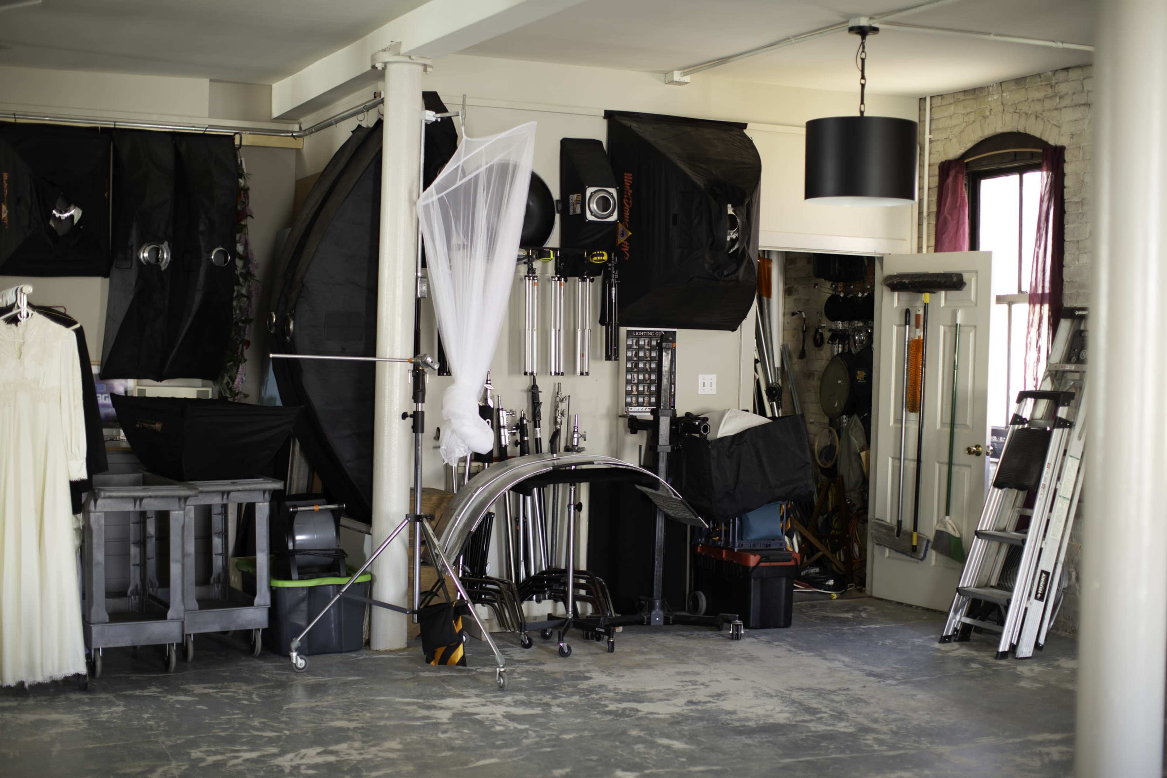 A photography studio filled with various equipment, including softboxes, backdrops, and a tall ladder against the wall.