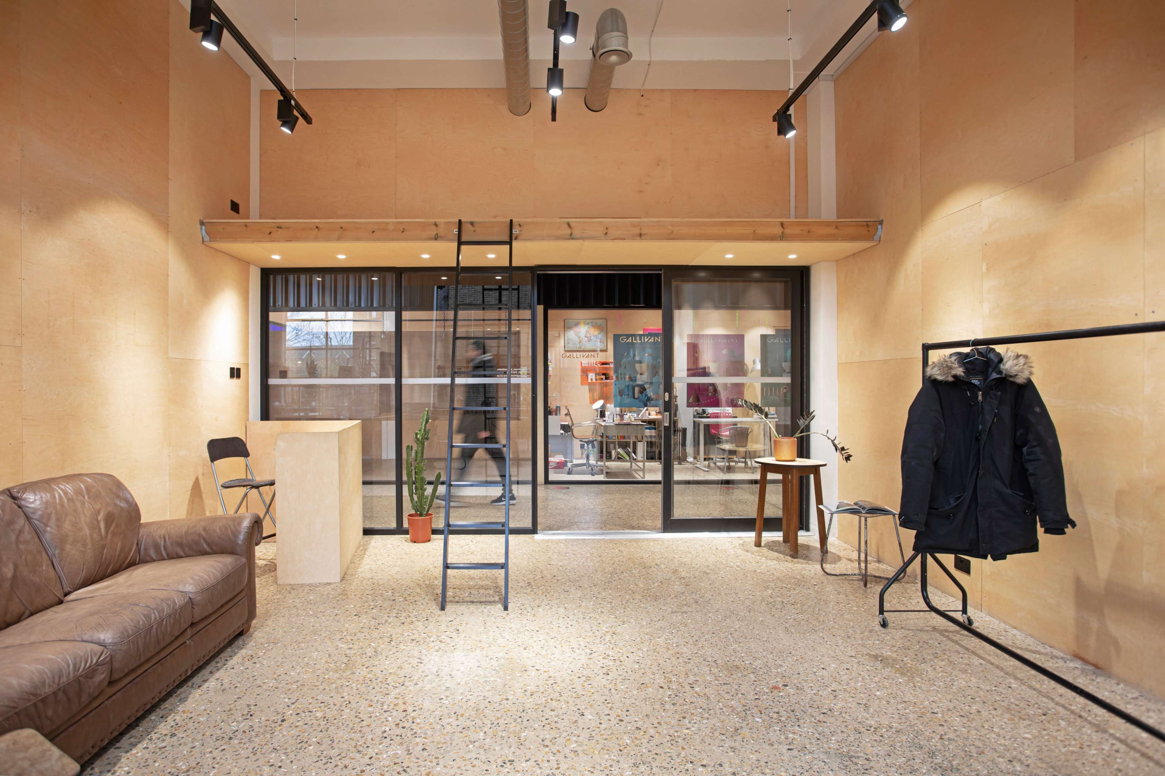 A modern interior space with wooden walls, a seating area featuring a brown couch, a ladder leading to a lofted area, and a clothing rack beside a potted plant.