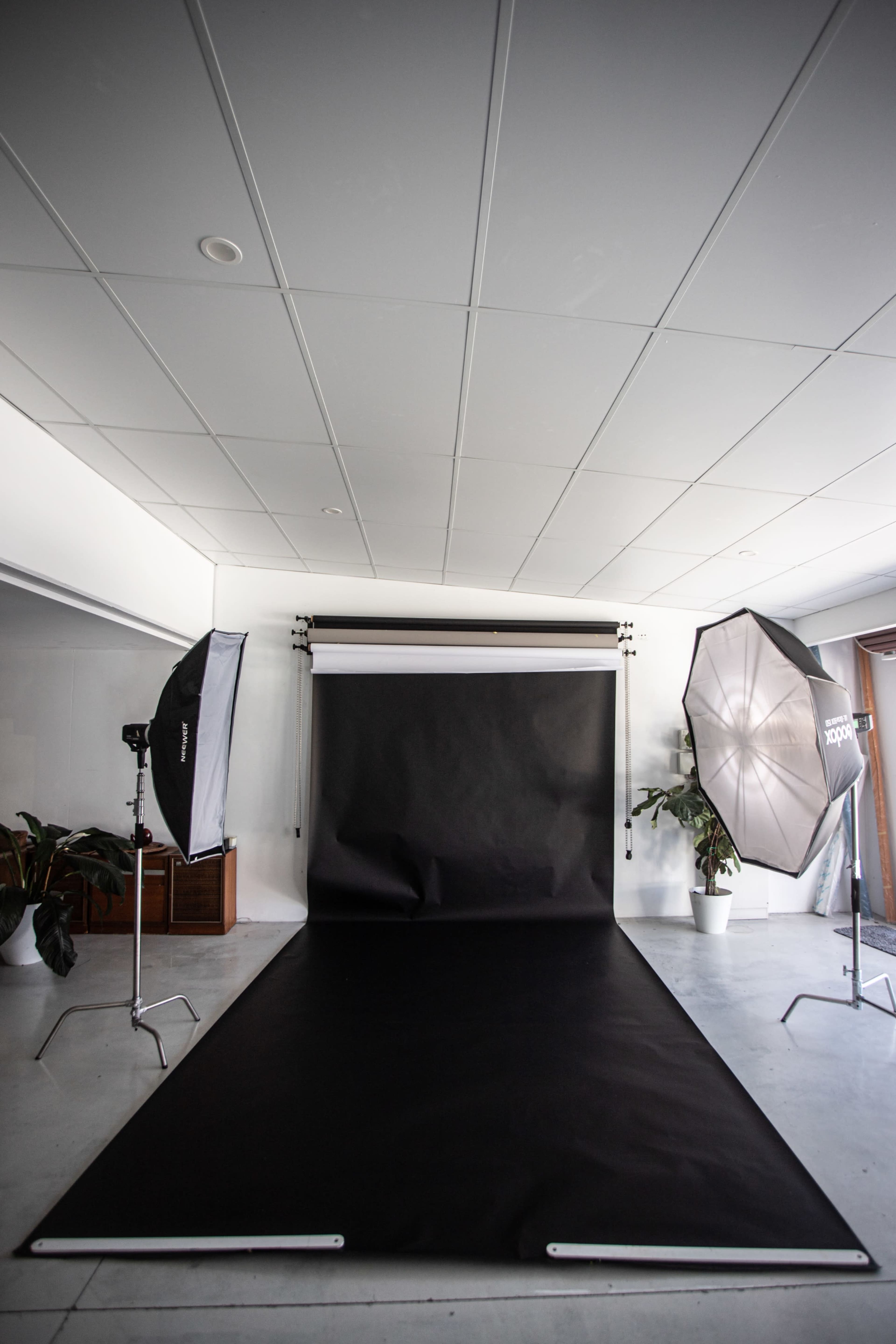 A photography studio features a black backdrops and lighting equipment set up on a gray floor.