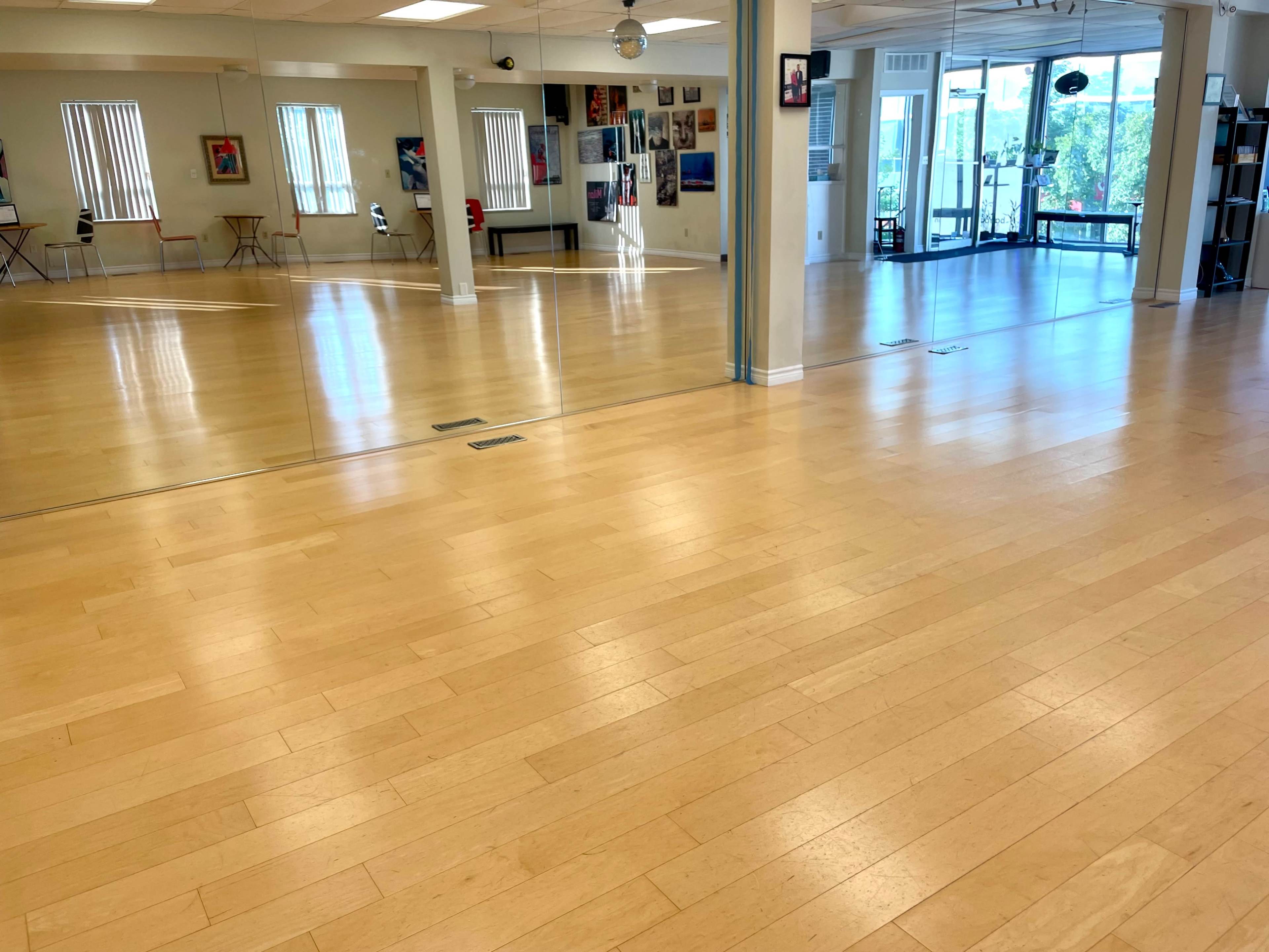 A spacious, well-lit studio with wooden floors, large mirrors, and various artworks on the walls.