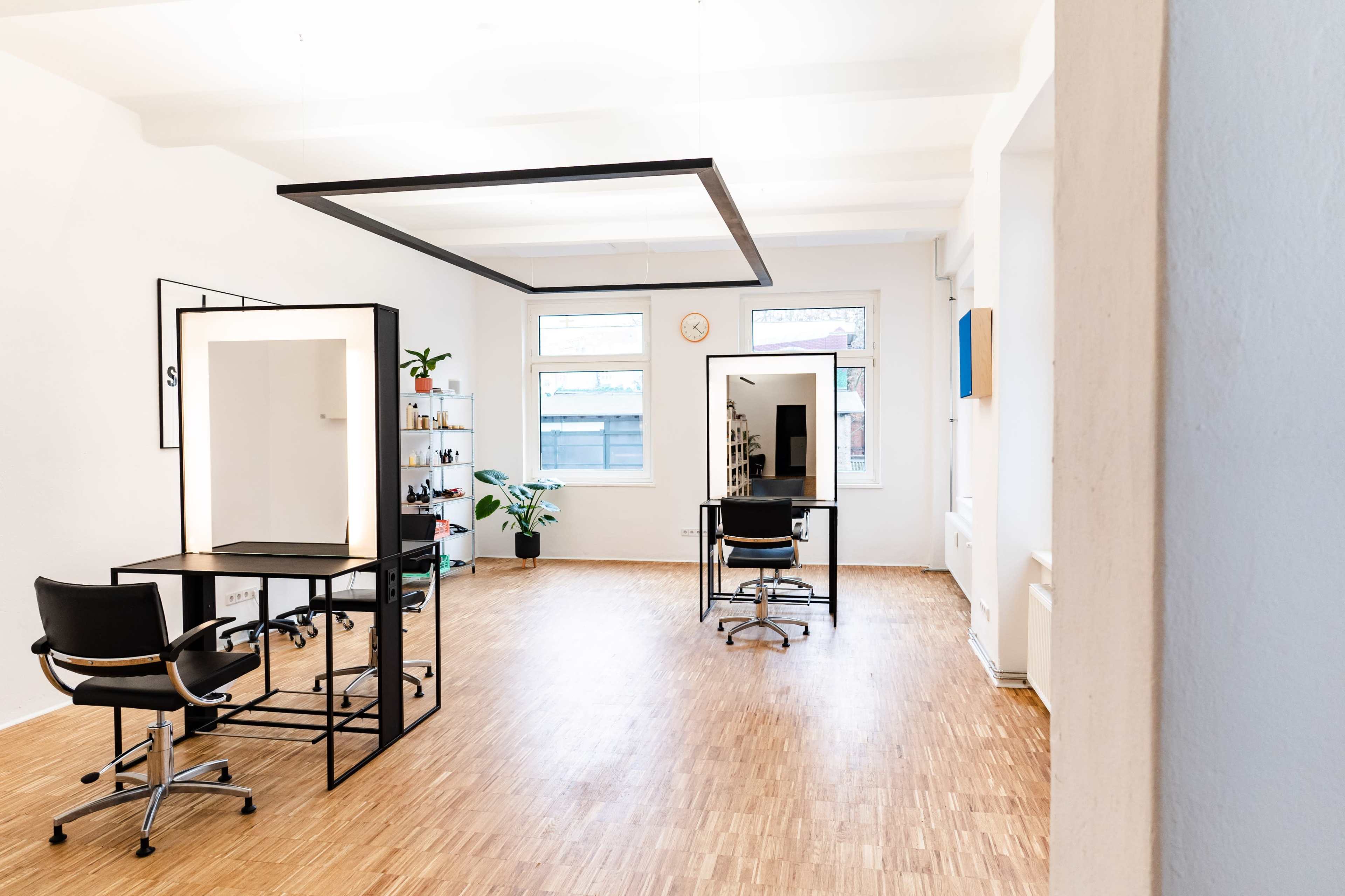 A spacious, minimalist office with desks, chairs, and large windows allowing natural light.