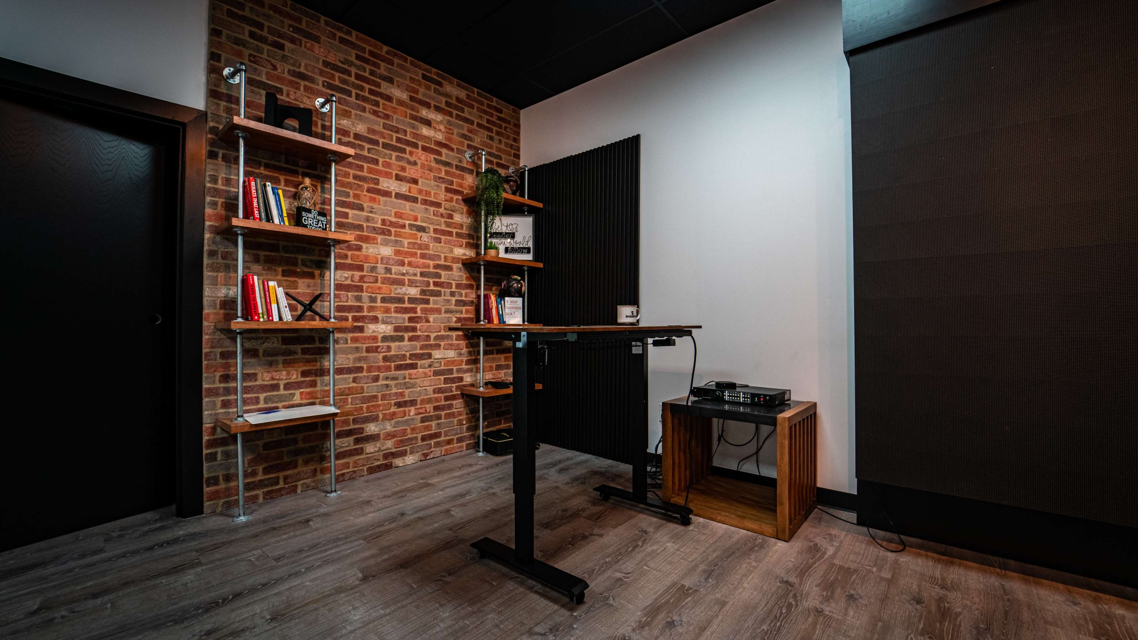 A modern workspace featuring a standing desk beside a wooden cabinet, with a brick accent wall and bookshelves displaying books and decorative items.