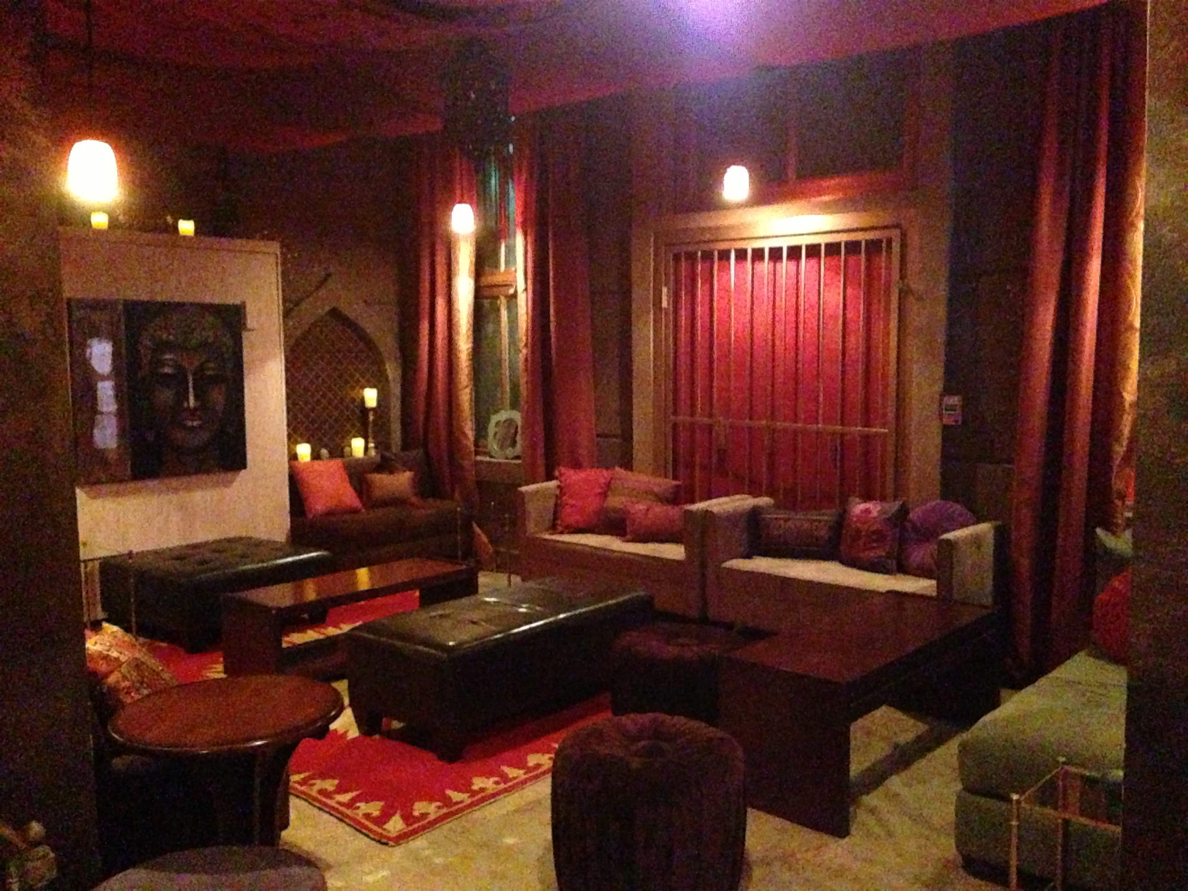 A dimly lit lounge area with various seating arrangements, rich textiles, and decorative elements including a wall art piece and candles.