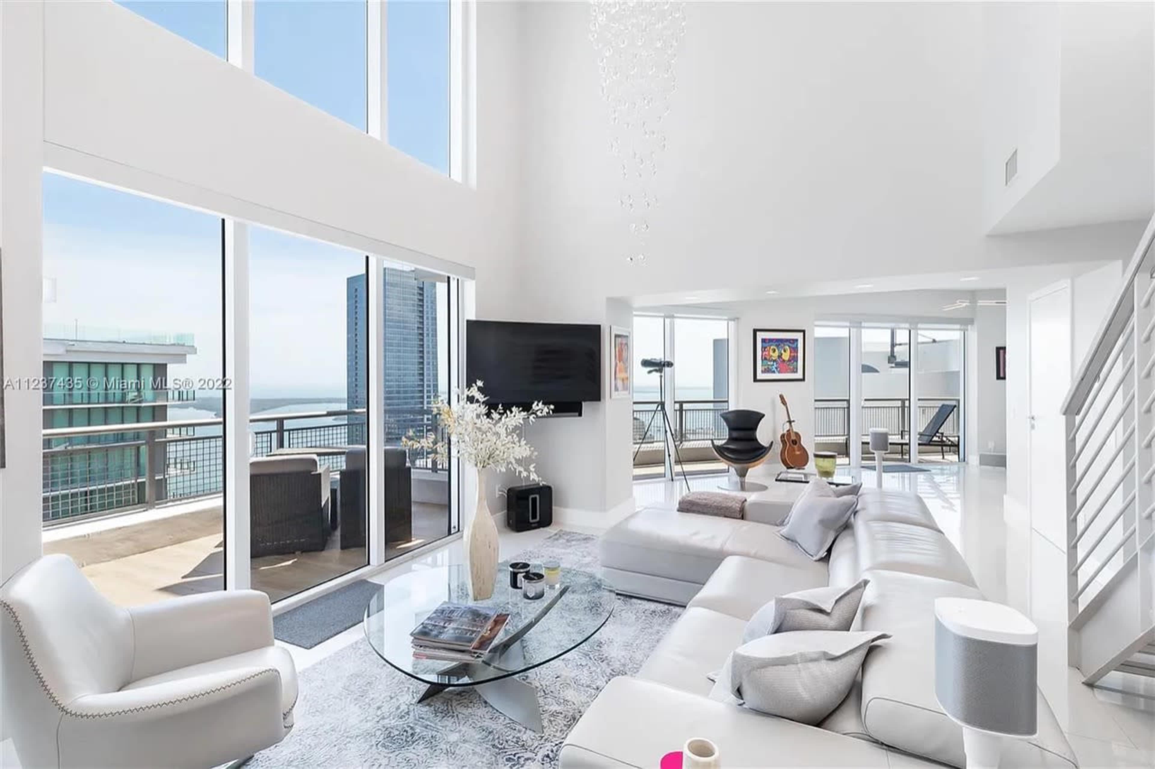 A modern, bright living room with large windows overlooking a city skyline and a balcony.
