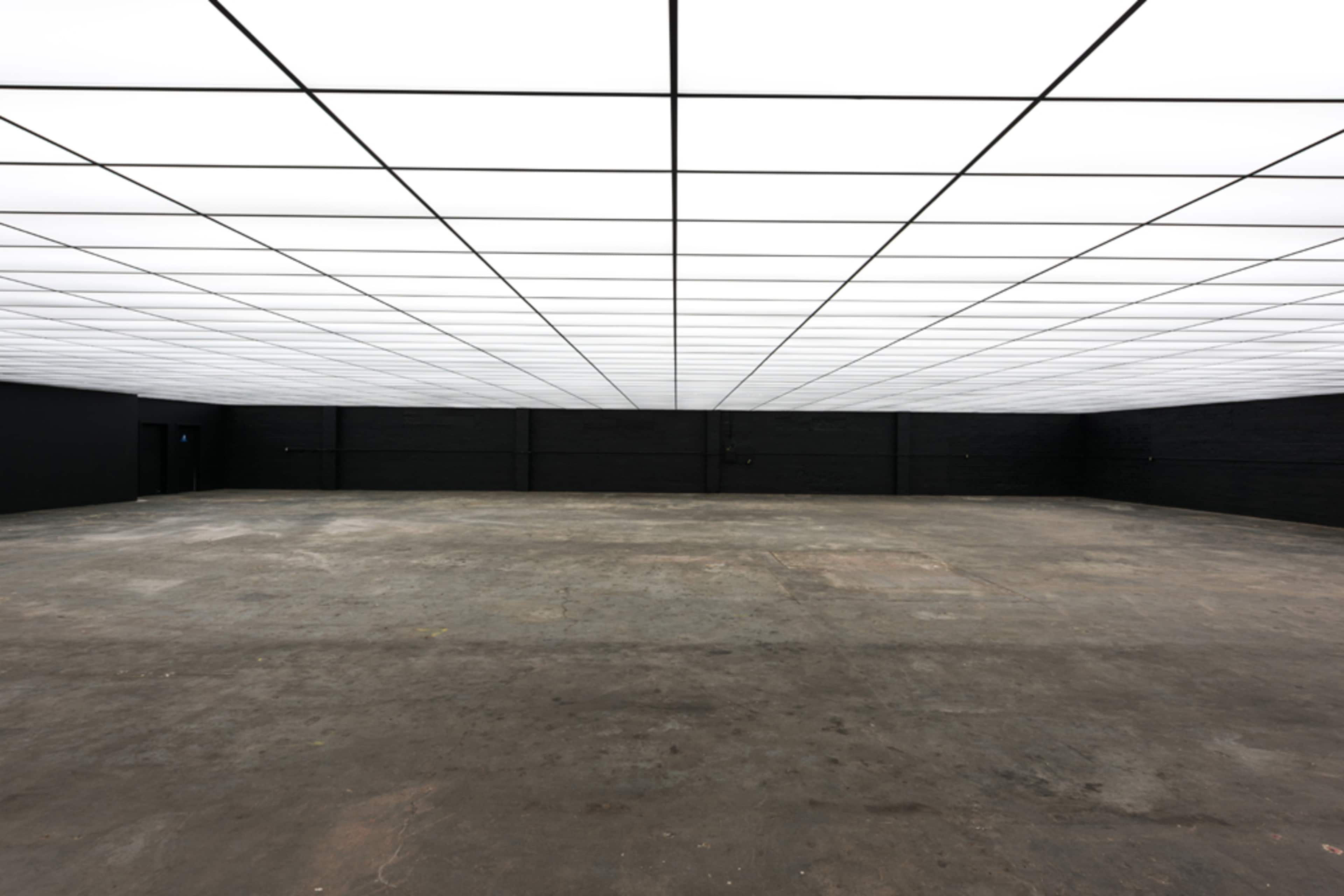 An empty industrial space with a flat, illuminated ceiling and dark walls.