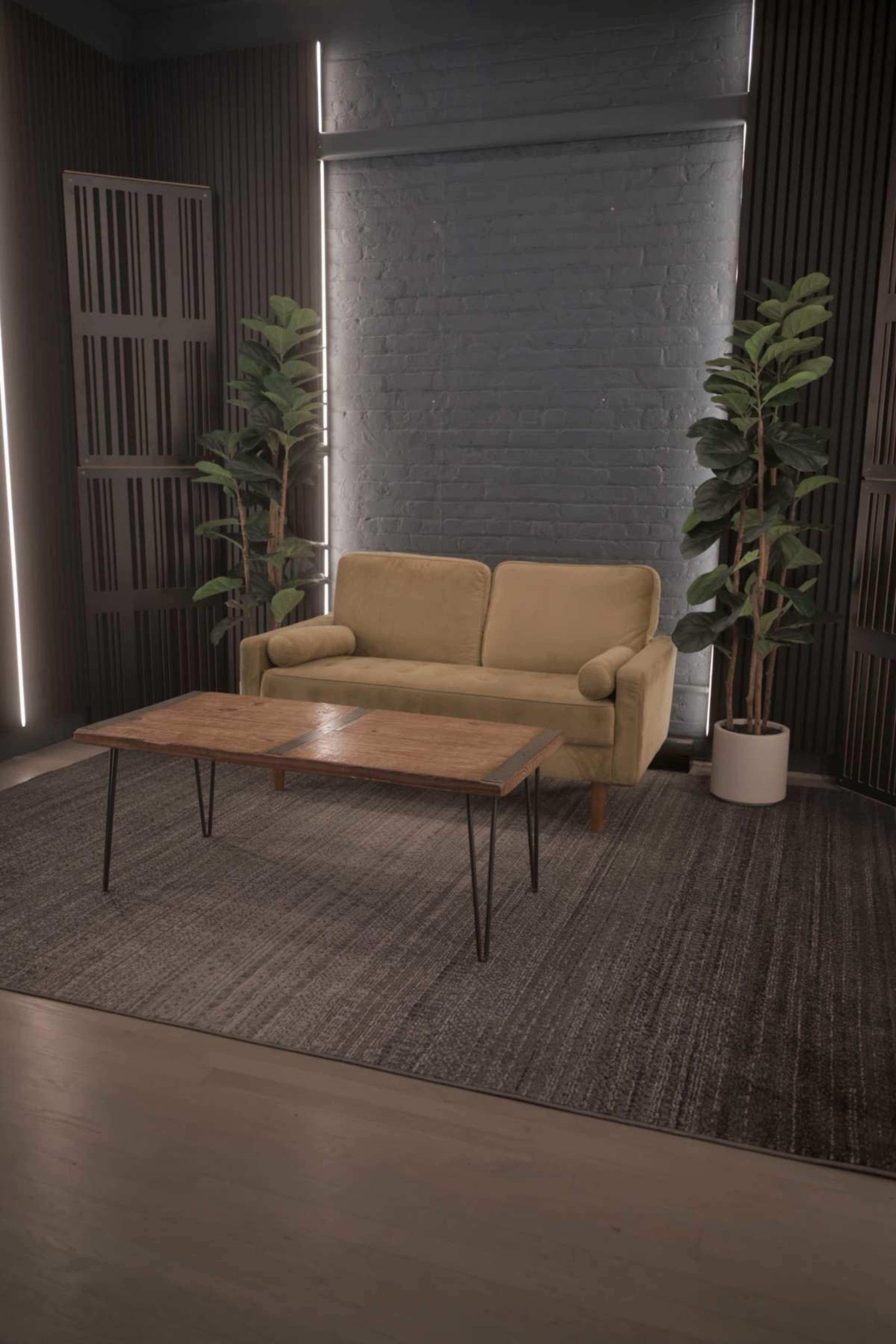 The image shows a modern living room setting with a beige couch and a wooden coffee table, surrounded by potted plants and accented by vertical light fixtures.