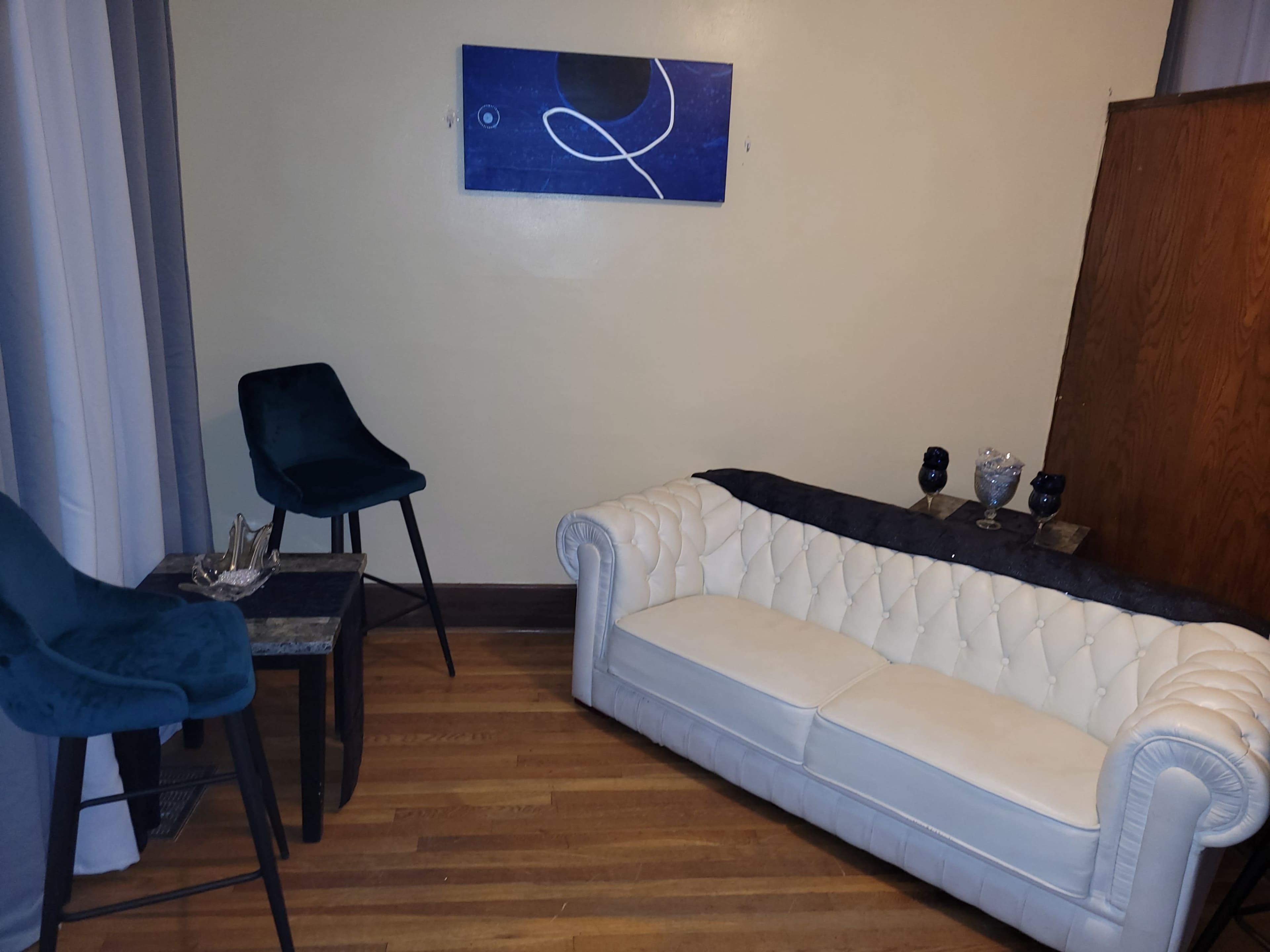 The room features a white tufted sofa, a black side table, and two blue upholstered chairs against a light-colored wall.