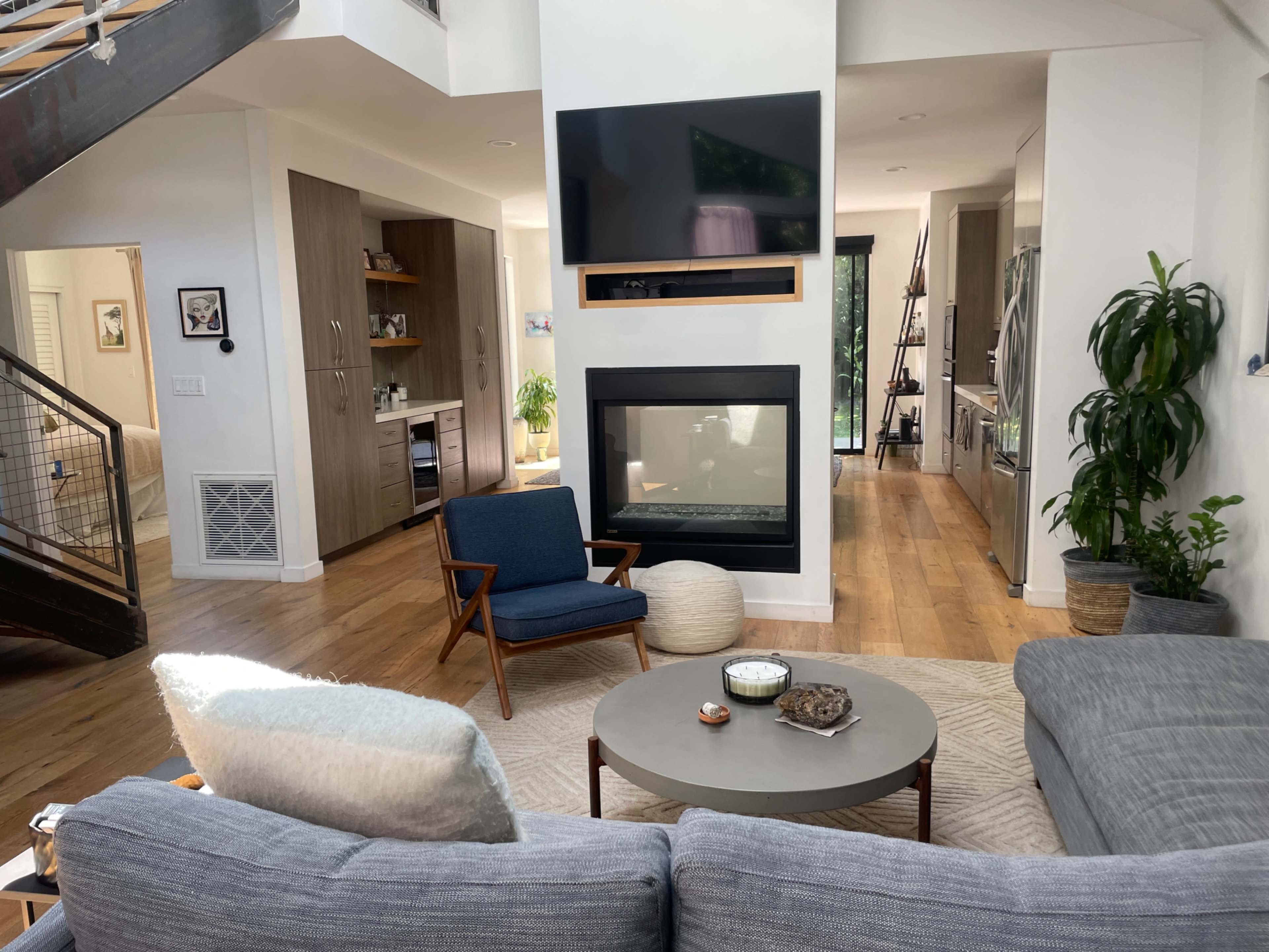 The image shows a modern living room featuring a central coffee table, a couch, an armchair, and a wall-mounted TV above a sleek fireplace.