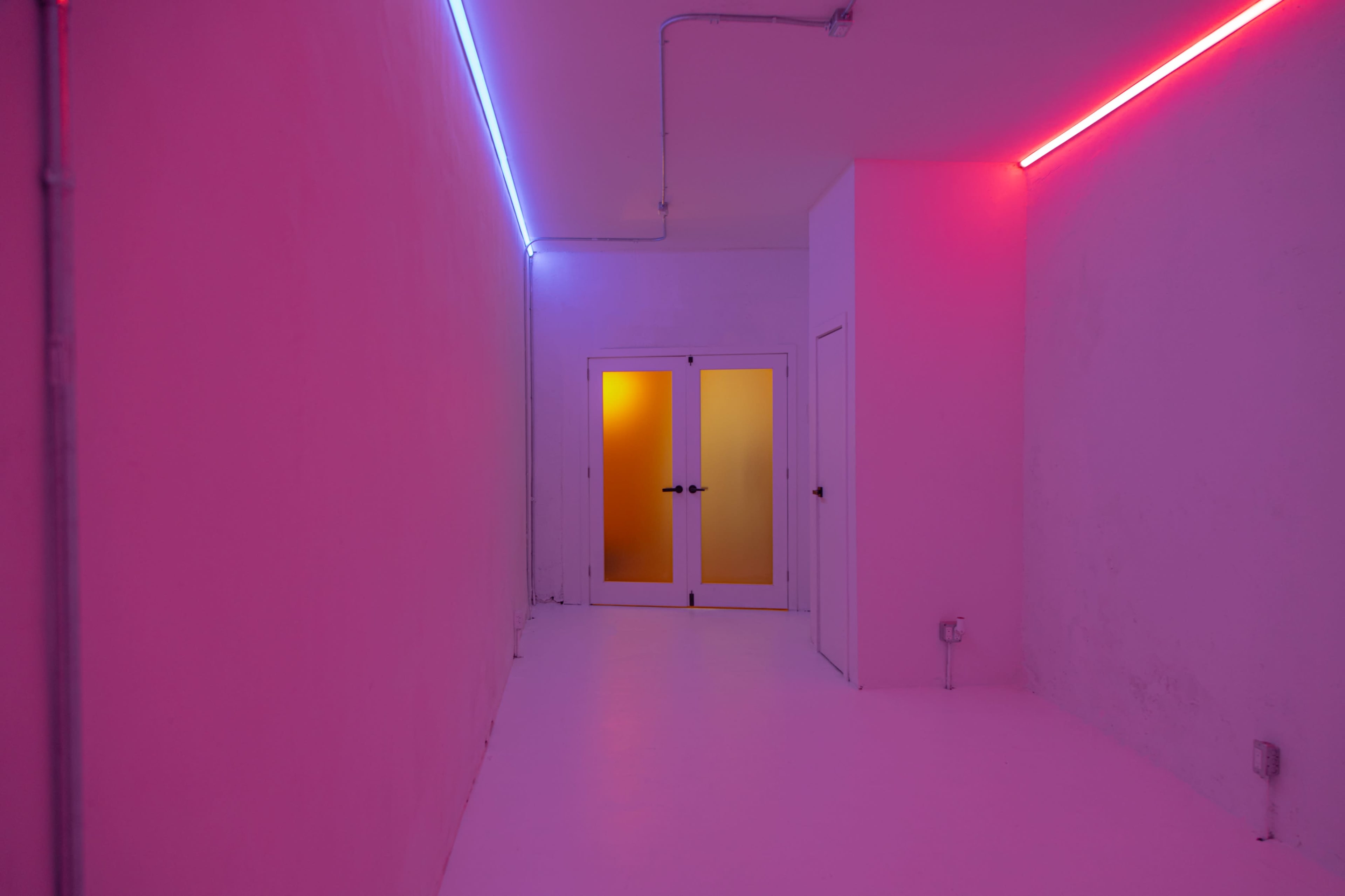 The image shows a minimalist room with purple and blue neon lights illuminating the walls, and a pair of double doors with frosted glass at the end of the hallway.