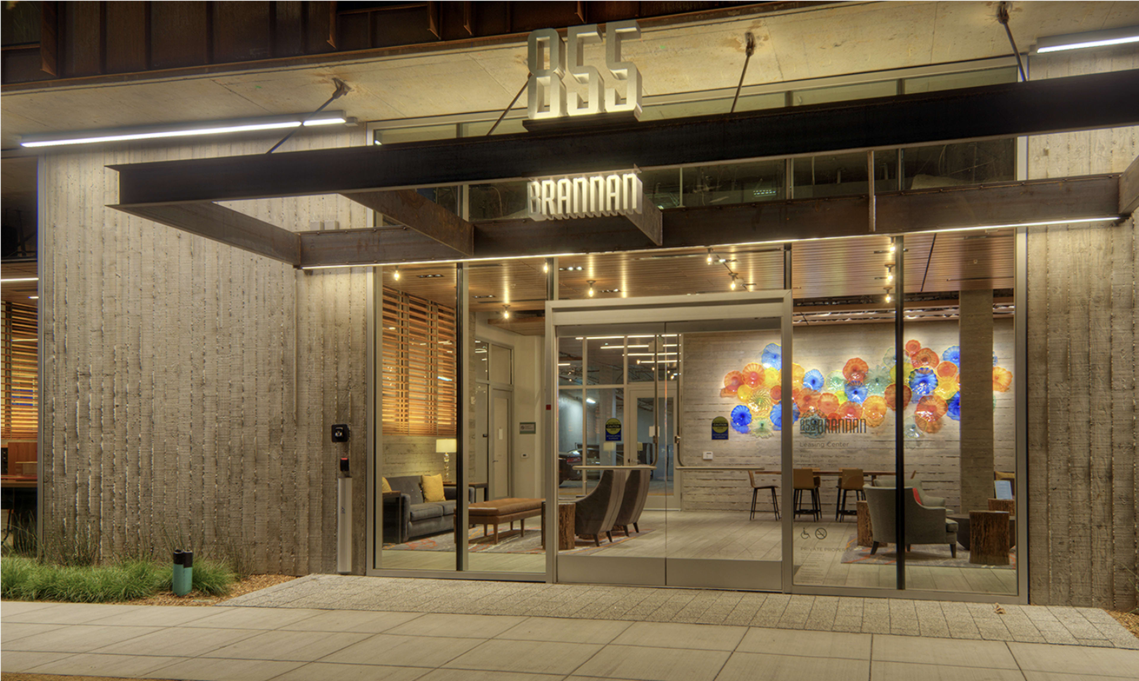 The image shows a modern building entrance with large glass windows, featuring a welcoming interior and a colorful art installation on the wall.