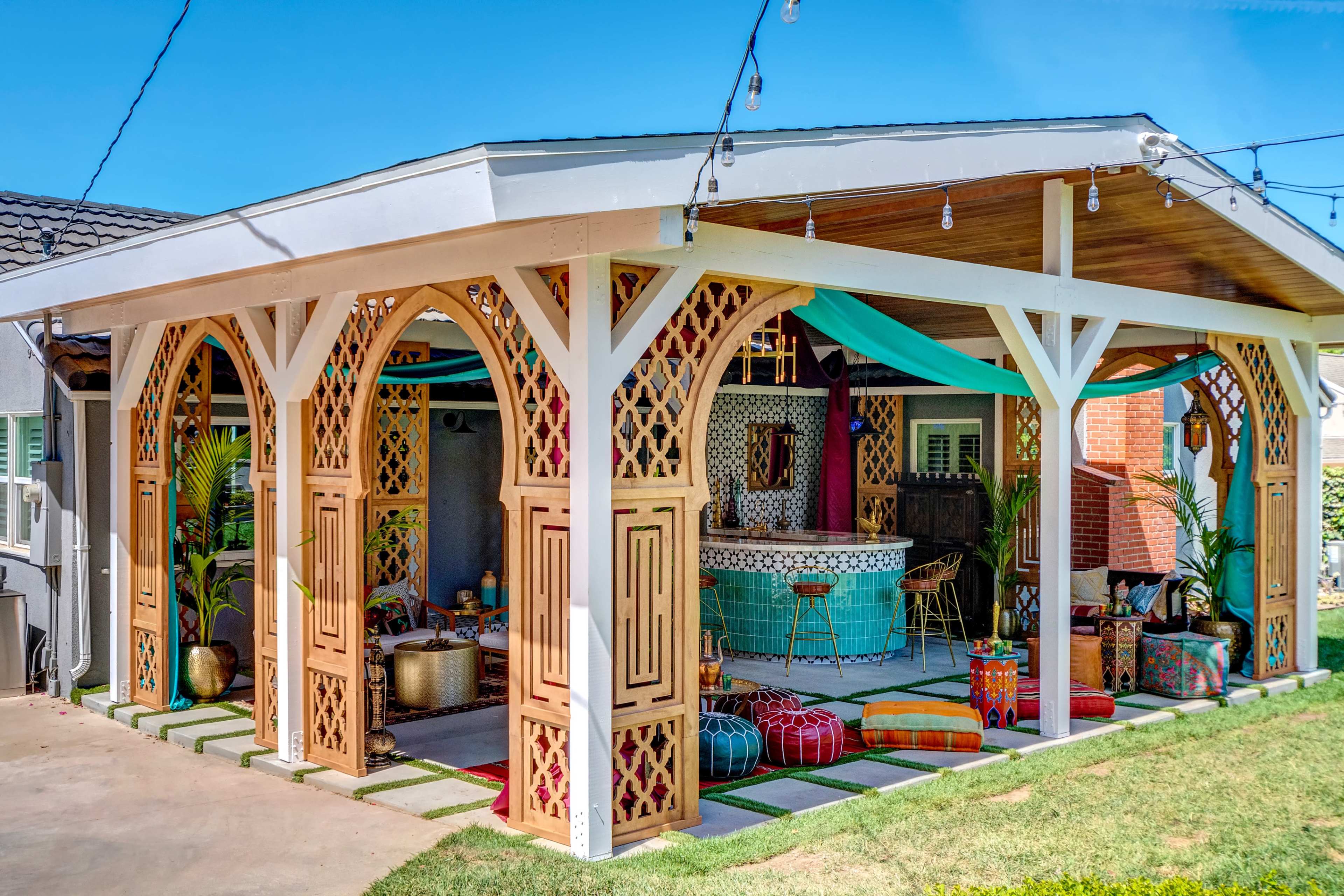 A covered outdoor space featuring intricate wooden latticework, colorful cushions, and a turquoise bar area adorned with tropical decor.