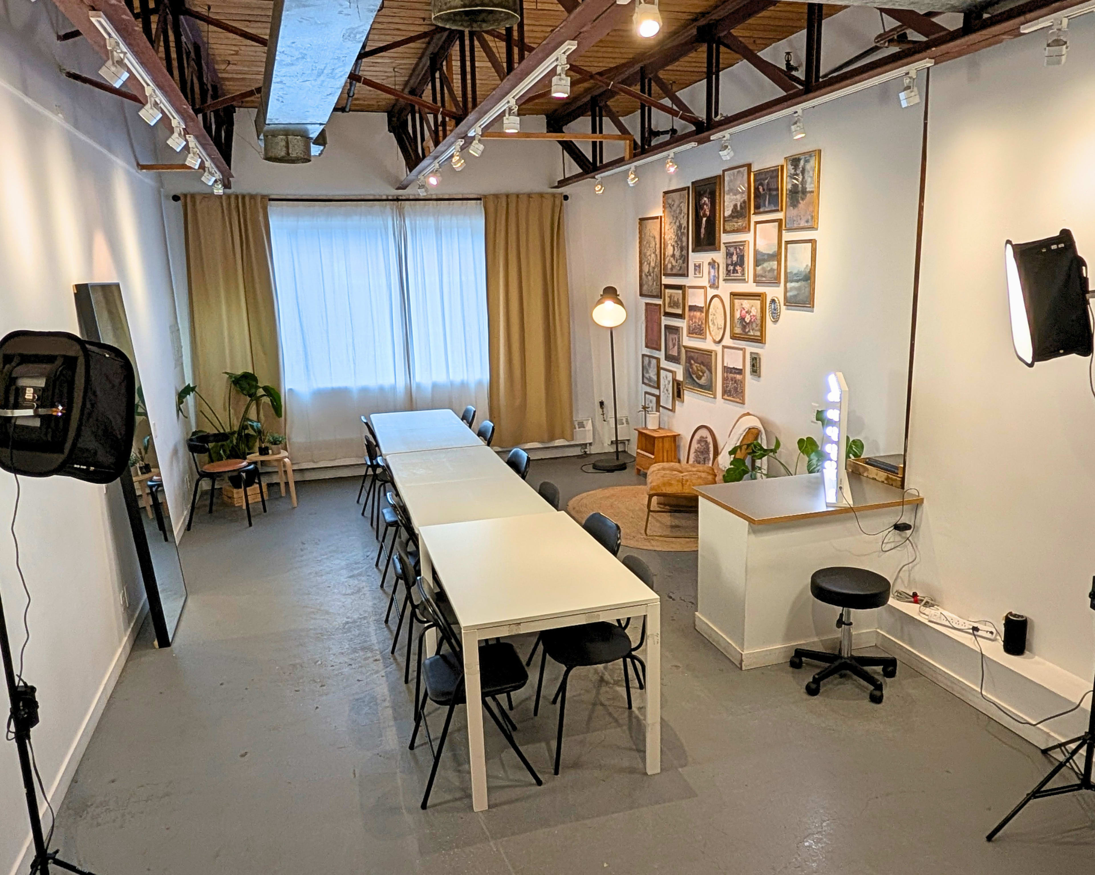 The image depicts a spacious, well-lit room with a long table surrounded by chairs, a lighted vanity area, and a wall adorned with framed pictures.
