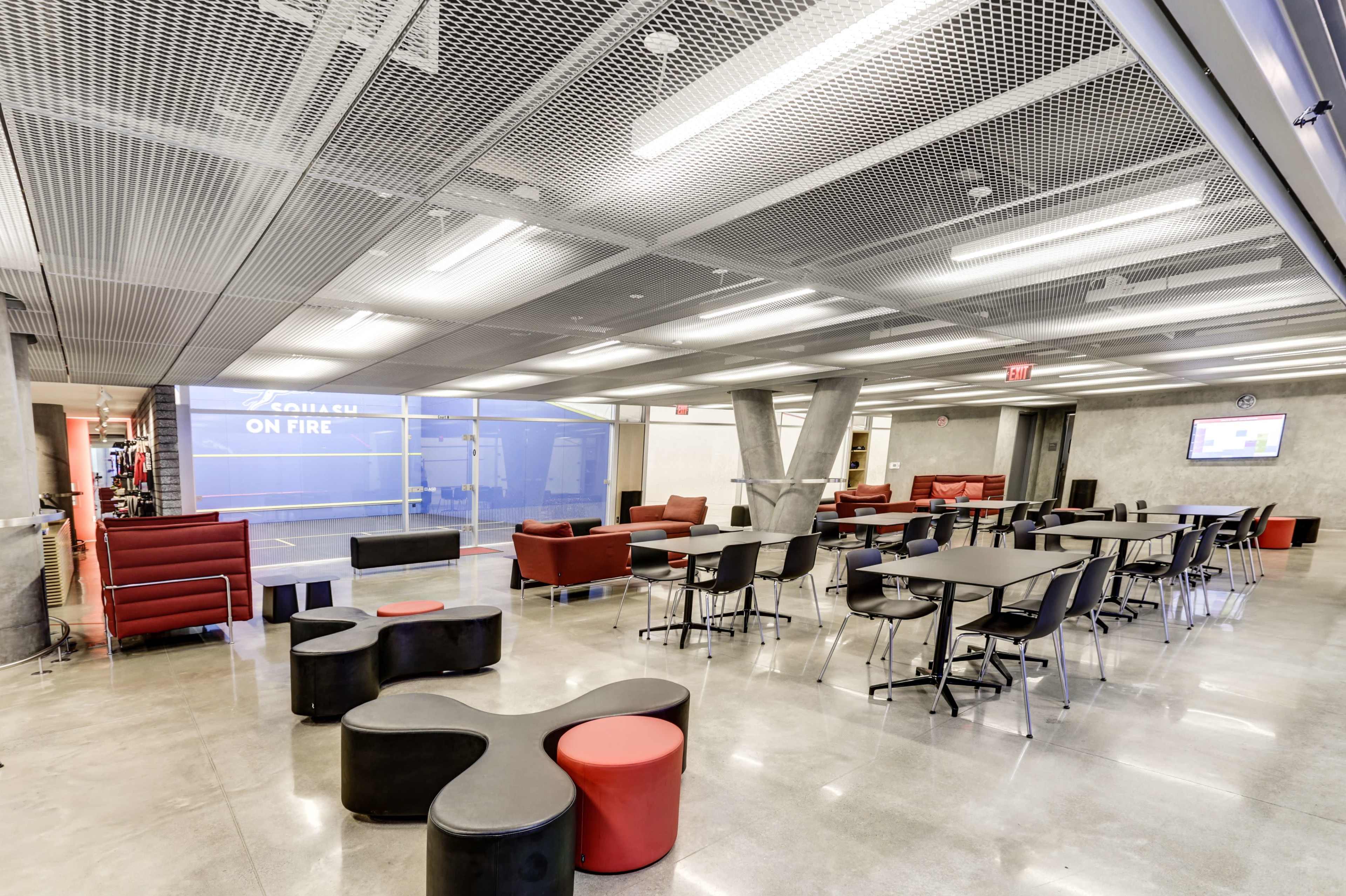 The image shows a modern lounge area with red and black seating, tables, and a glass wall with “ON FIRE” written on it.