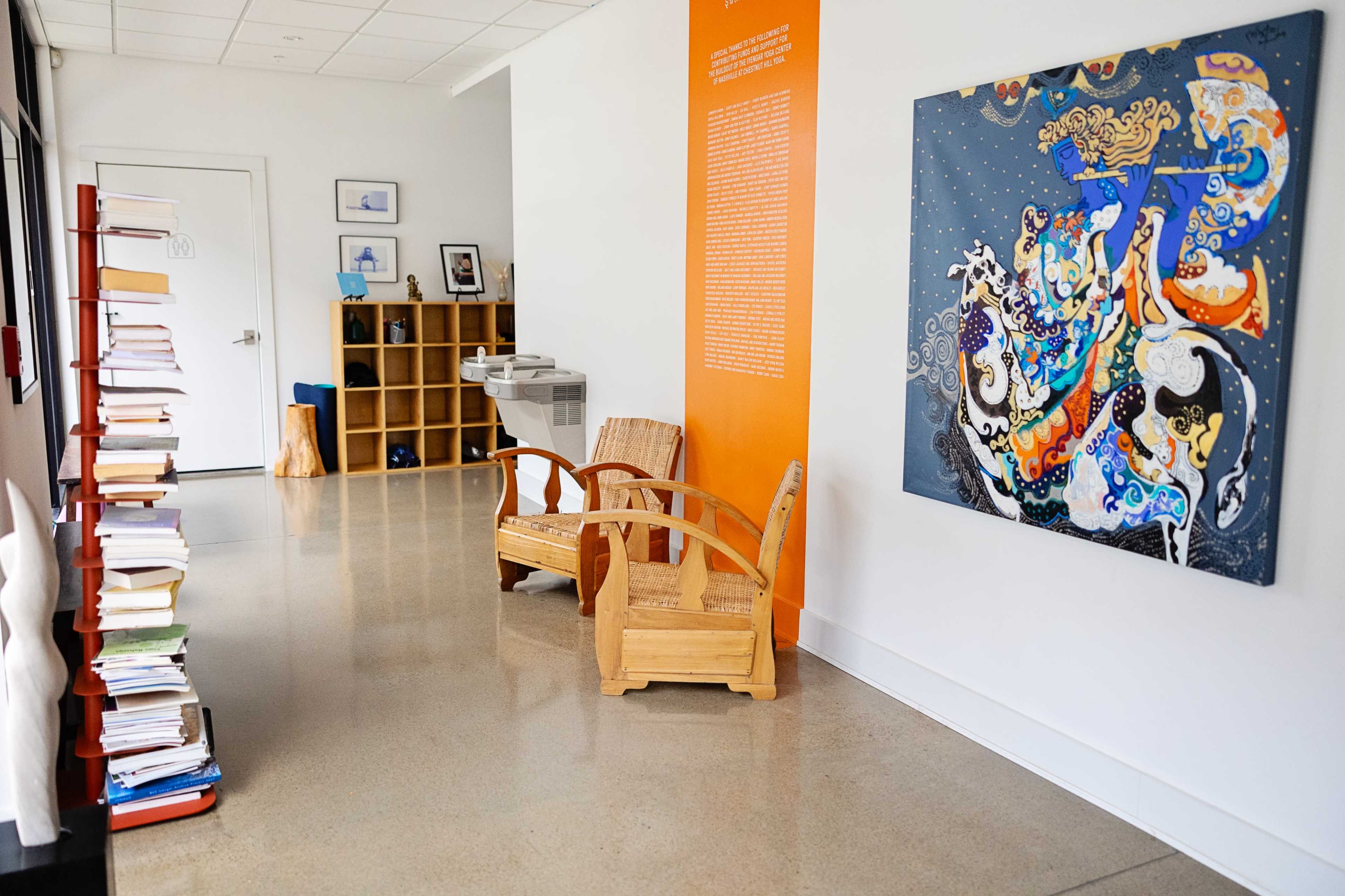 A hallway features wooden chairs, a vibrant artwork on the wall, and bookshelves filled with books.