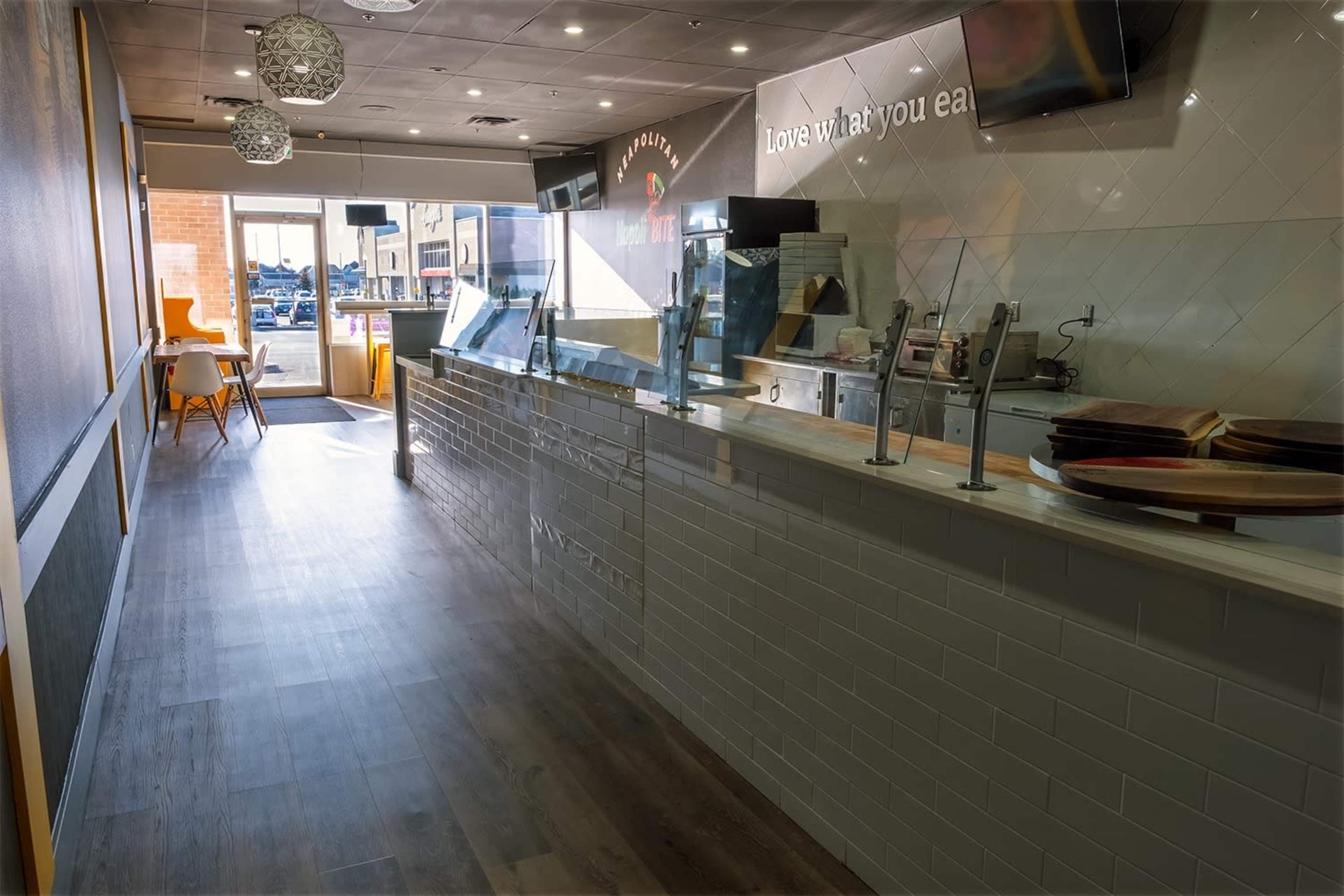 The interior of a modern, brightly lit restaurant with a counter display and seating area, leading to an entrance.