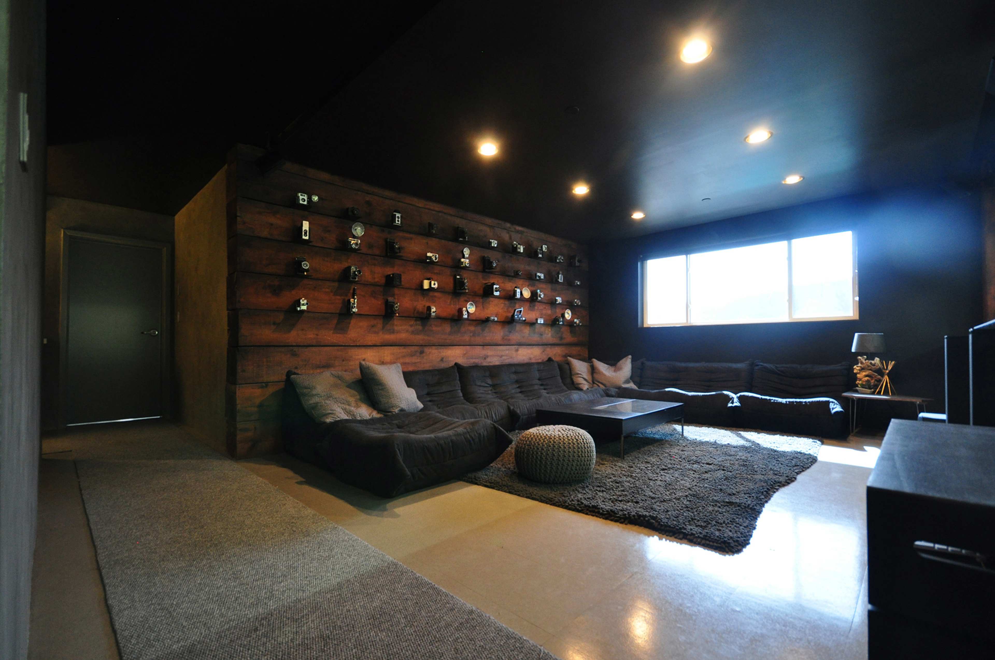 A modern living room featuring a dark color scheme, a large sofa, a coffee table, and a wall adorned with various camera lenses.